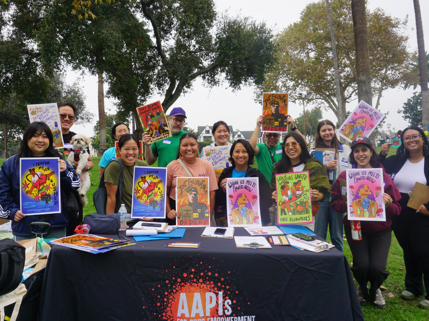 Group of diverse people at an outdoor advocacy event holding colorful protest signs supporting climate action and social justice, with trees and a building in the background.