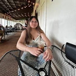 A woman sitting at a table in a cafe, holding a drink with a straw, inside a well-lit, modern establishment.