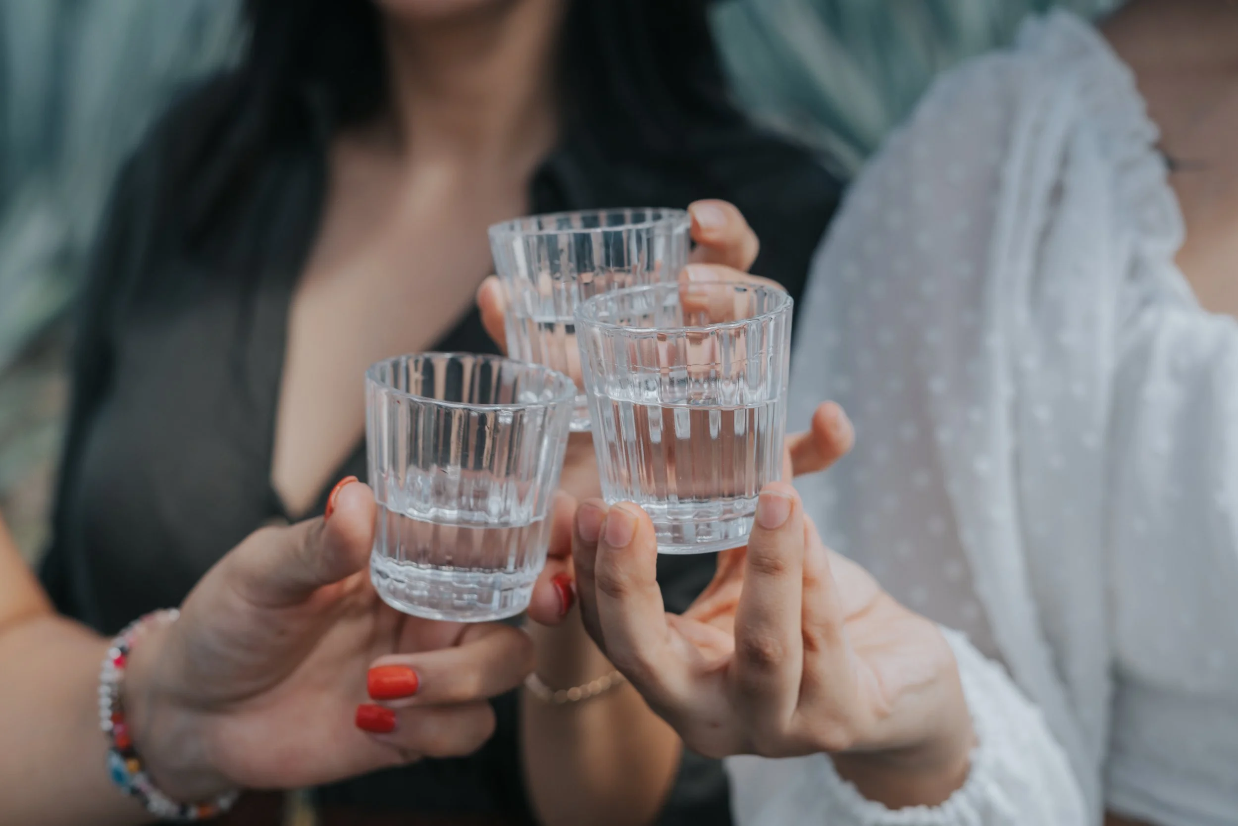Varias personas sosteniendo vasos cortos de cristal con Mezcal, en un brindis en un ambiente social.