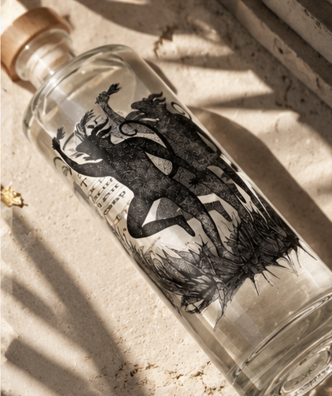 Botella de Mezcal  Joven Artesanal marca 9 Espíritus Mezcal de la variedad de agave Arroqueño transparente con ilustraciones de chanques y seres místicos en negro, en un espacio con luz solar y sombras sobre una superficie de piedra o concreto.