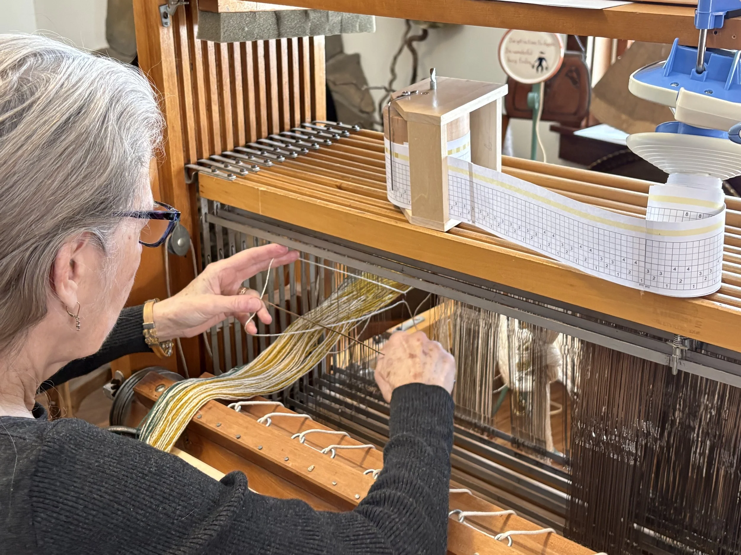 Weaver pulling a thread through the eye of a heddle