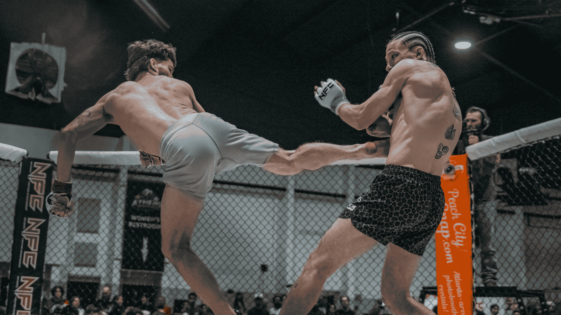 Two mixed martial arts fighters engaged in a fight inside a cage, one delivering a kick to the other.