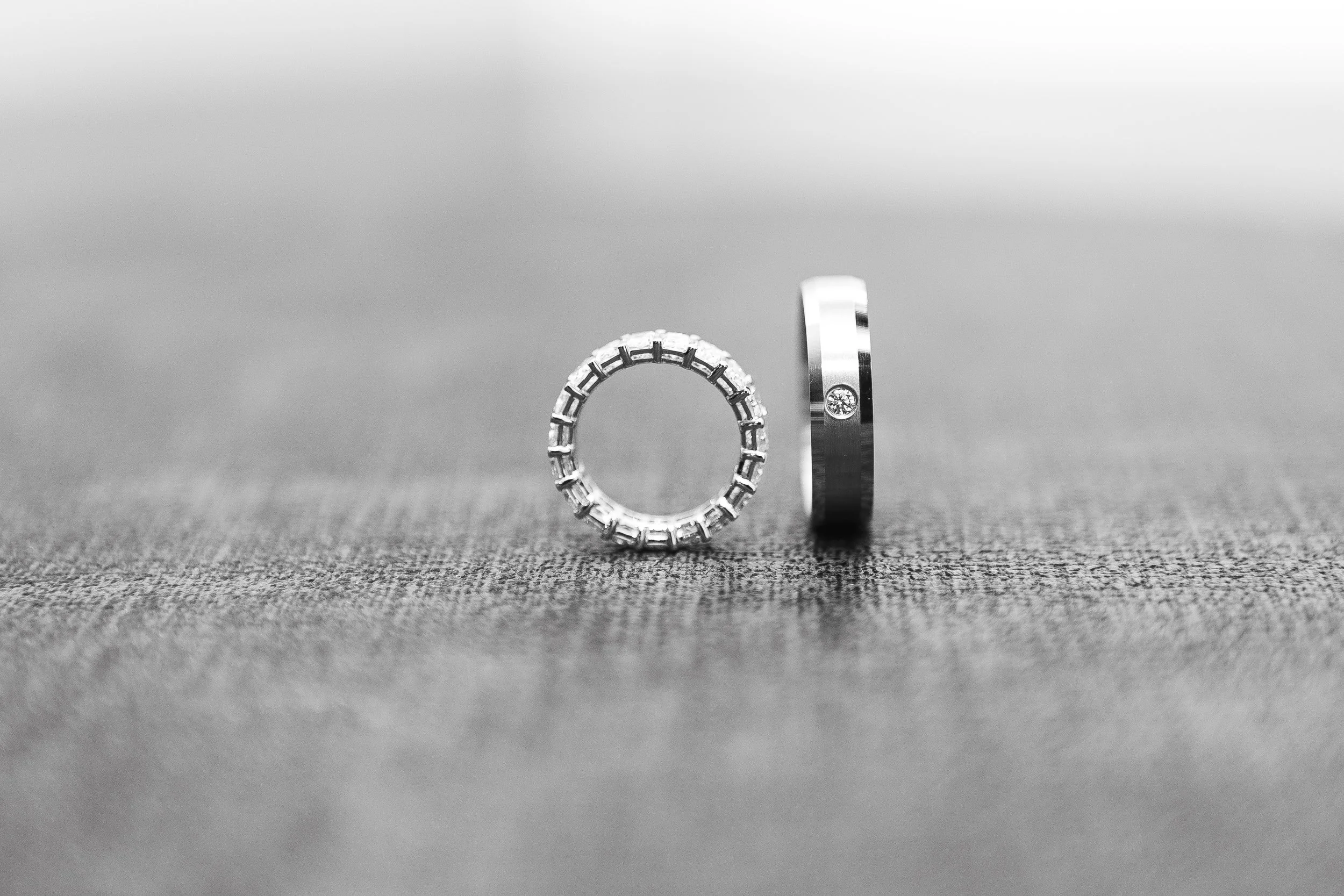 A diamond ring standing upright on a flat surface beside a wedding band.