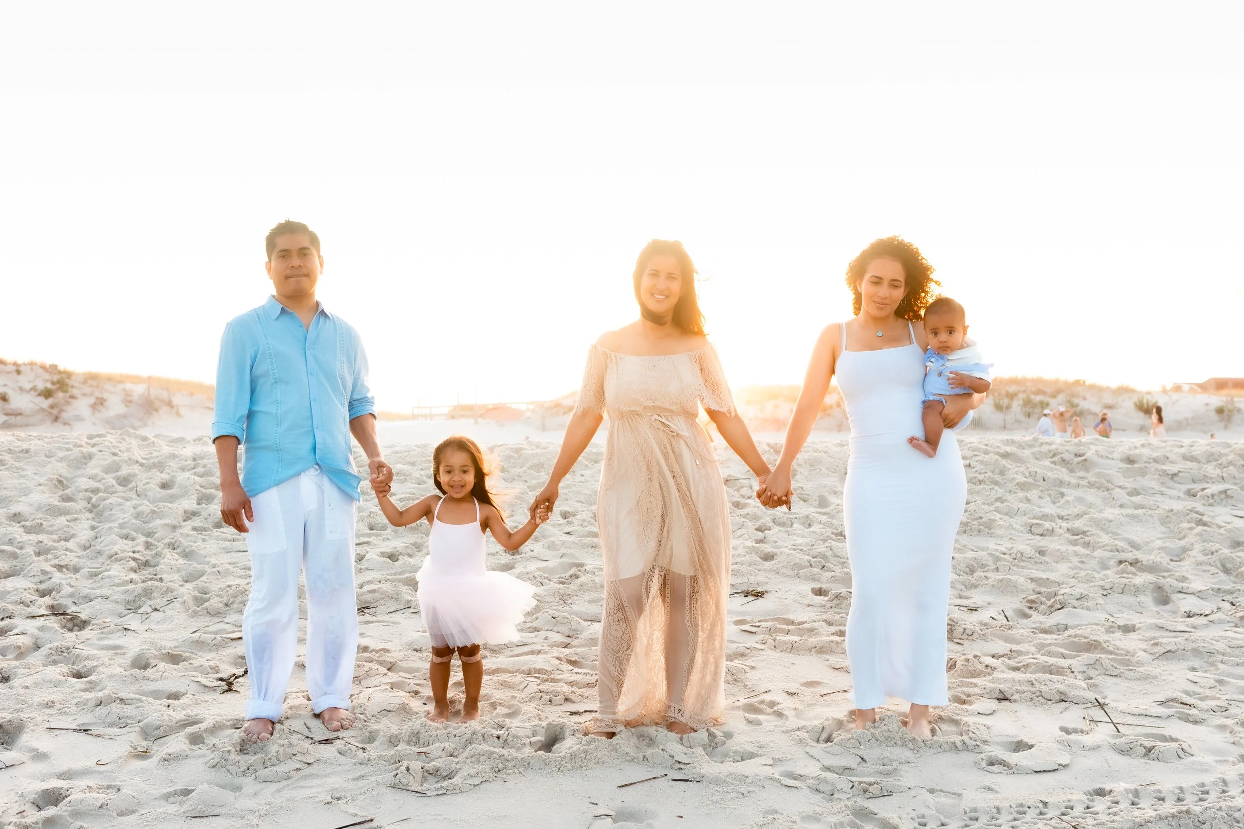 A family walking on the beach at sunset, holding hands, dressed in casual summer clothing.
