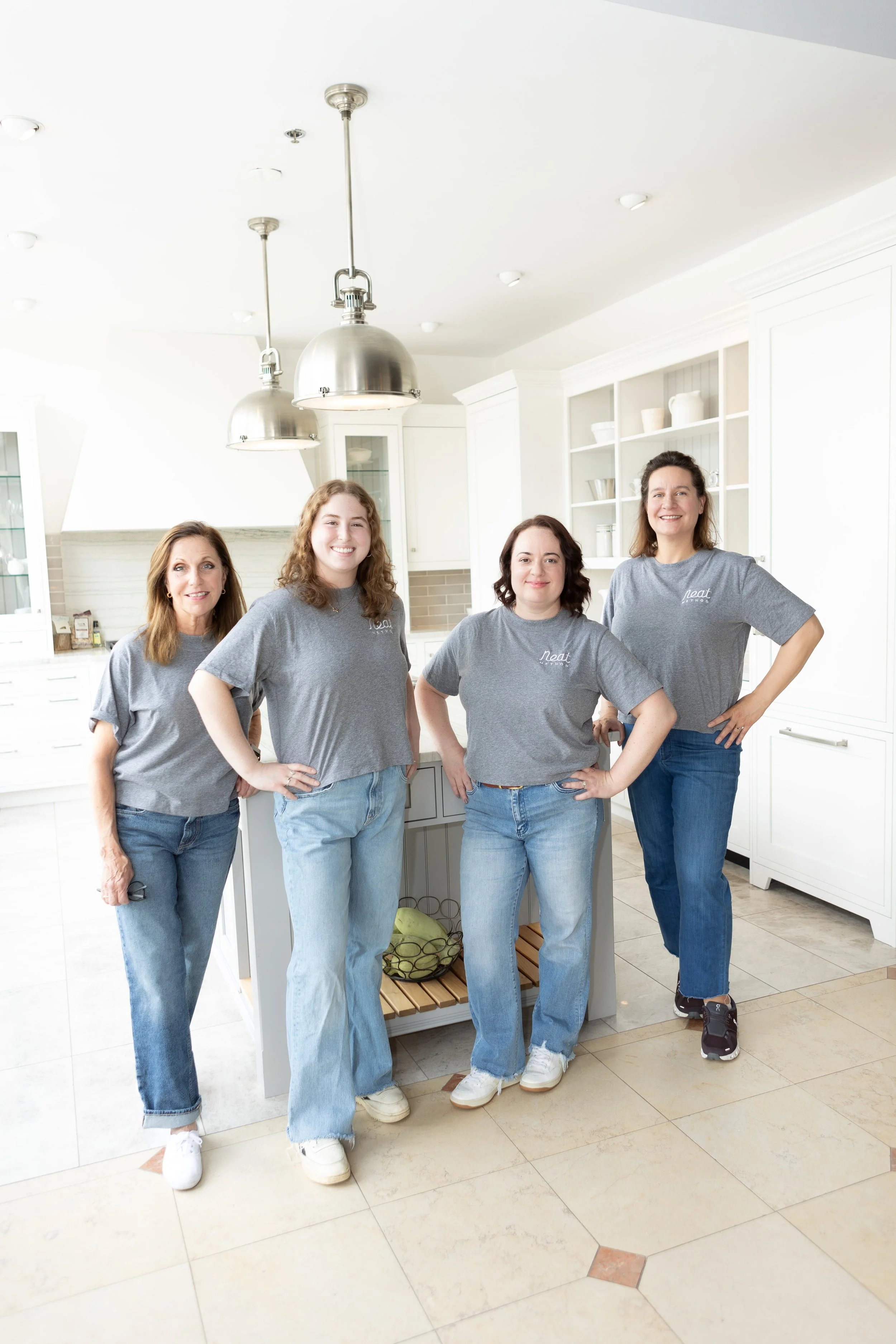 Four women from Neat Method Bergen County standing in a bright, modern kitchen, wearing matching gray t-shirts, smiling at the camera.