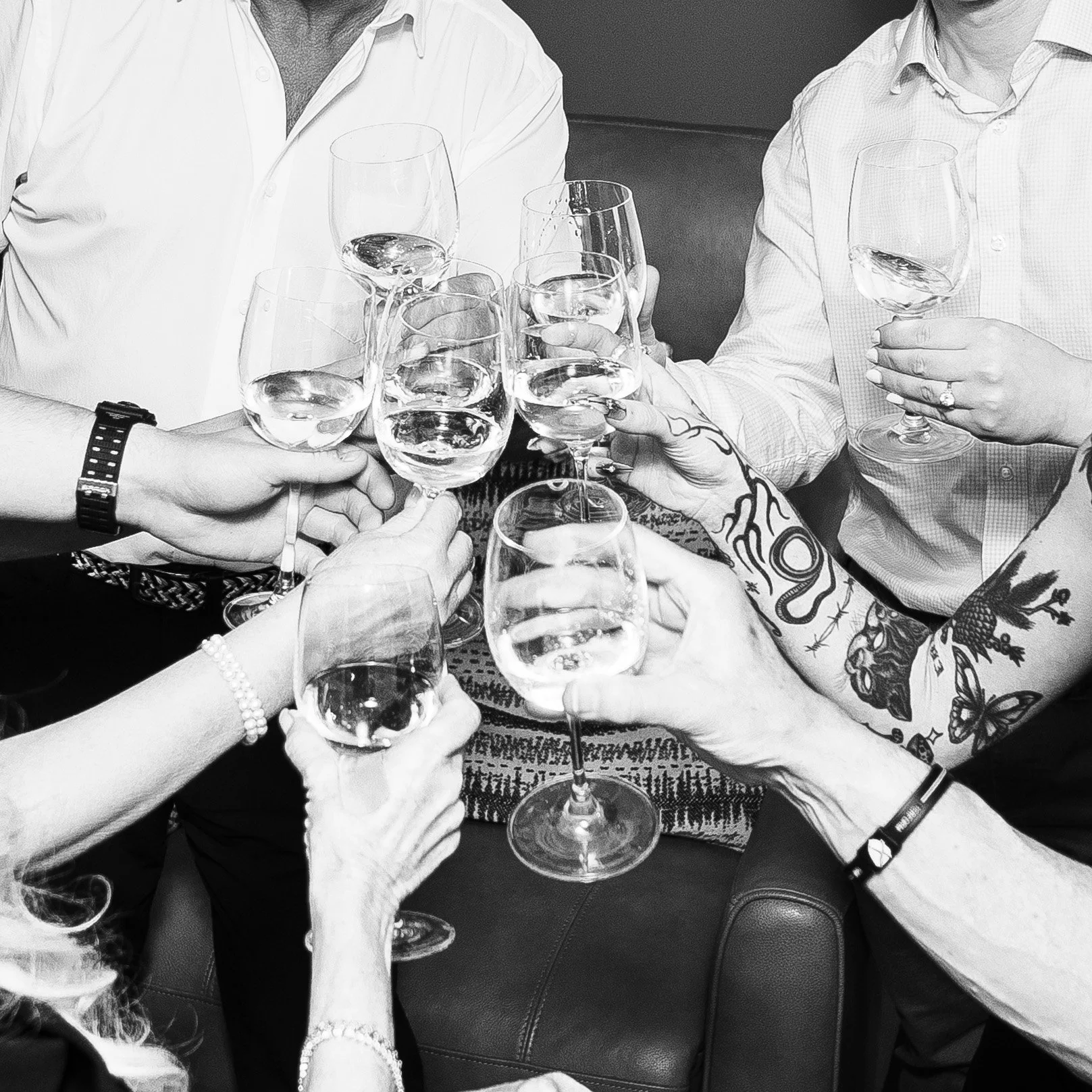 Several people toasting with wine glasses filled with white wine, seen from a close angle with hands and arms in focus.