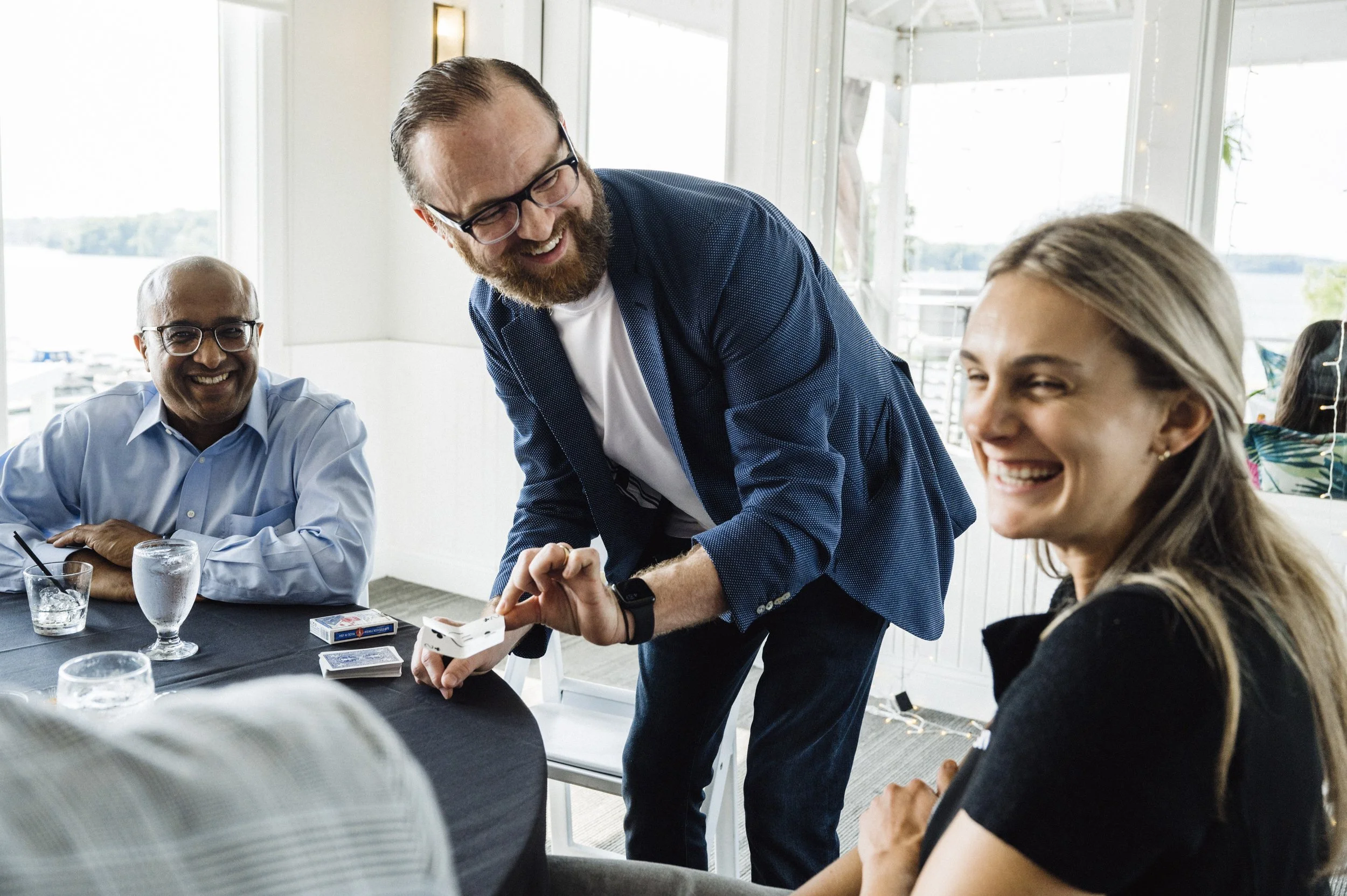 A man performing a card trick for a group of people at a table during a social gathering.