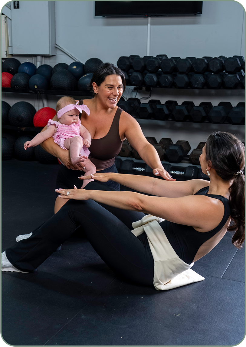 HERPhase Emma Scrench Holding Baby While Client Performs Ab Crunch In Gym