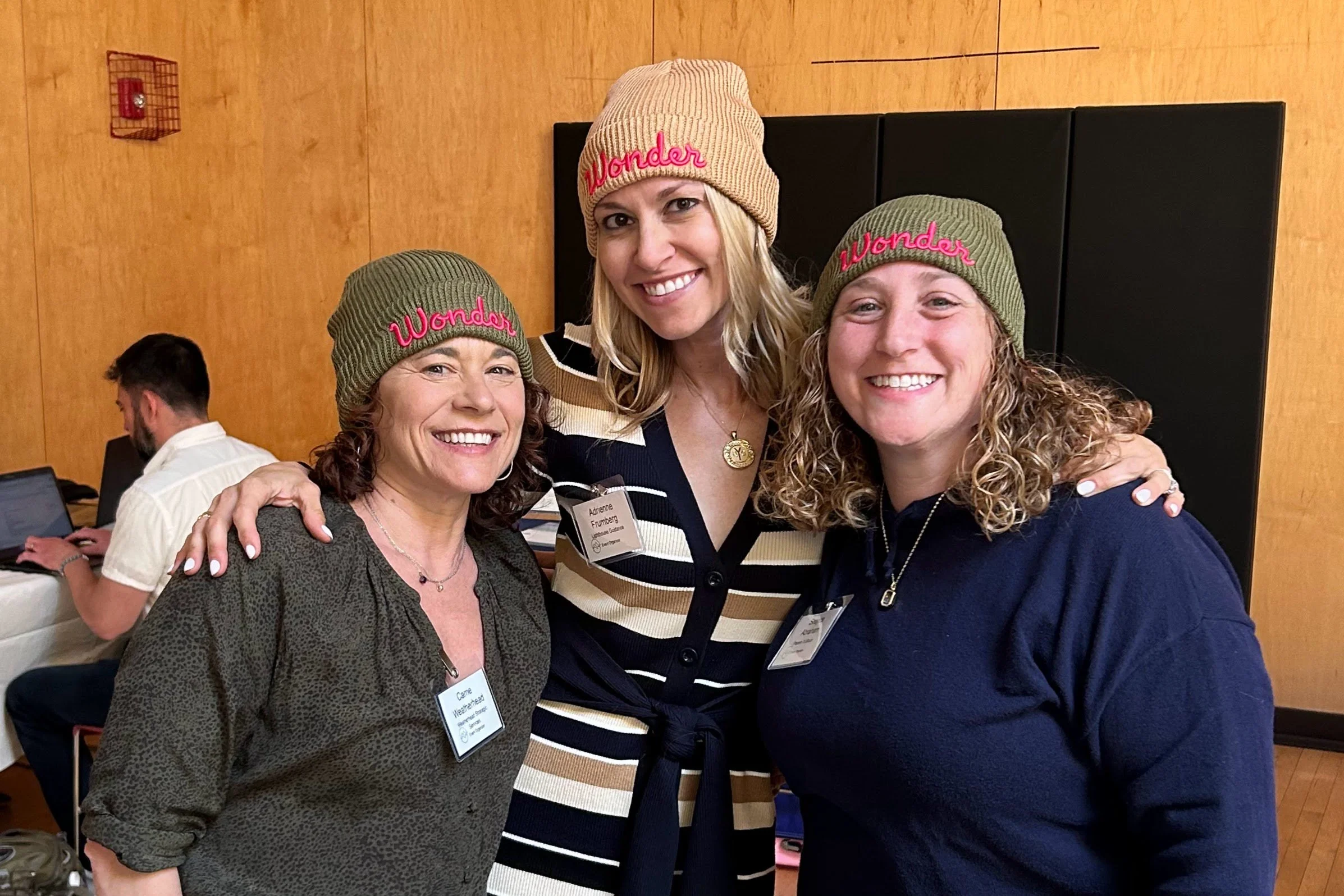 Three women smiling wearing beanies and standing close together
