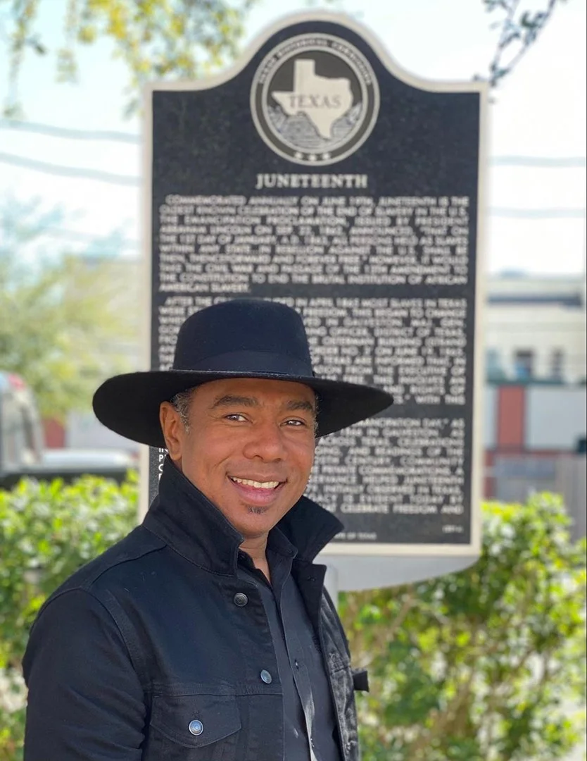 Person wearing a black hat and jacket standing in front of a Juneteenth historical marker in Texas.