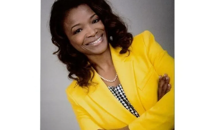 Smiling person in yellow blazer with crossed arms.