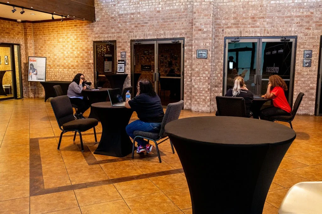 People sitting at round tables in a brick-walled room with glass doors and chairs.