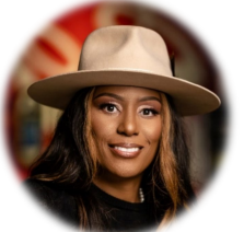 Person wearing a wide-brimmed hat, smiling, with long hair, in a blurred background.