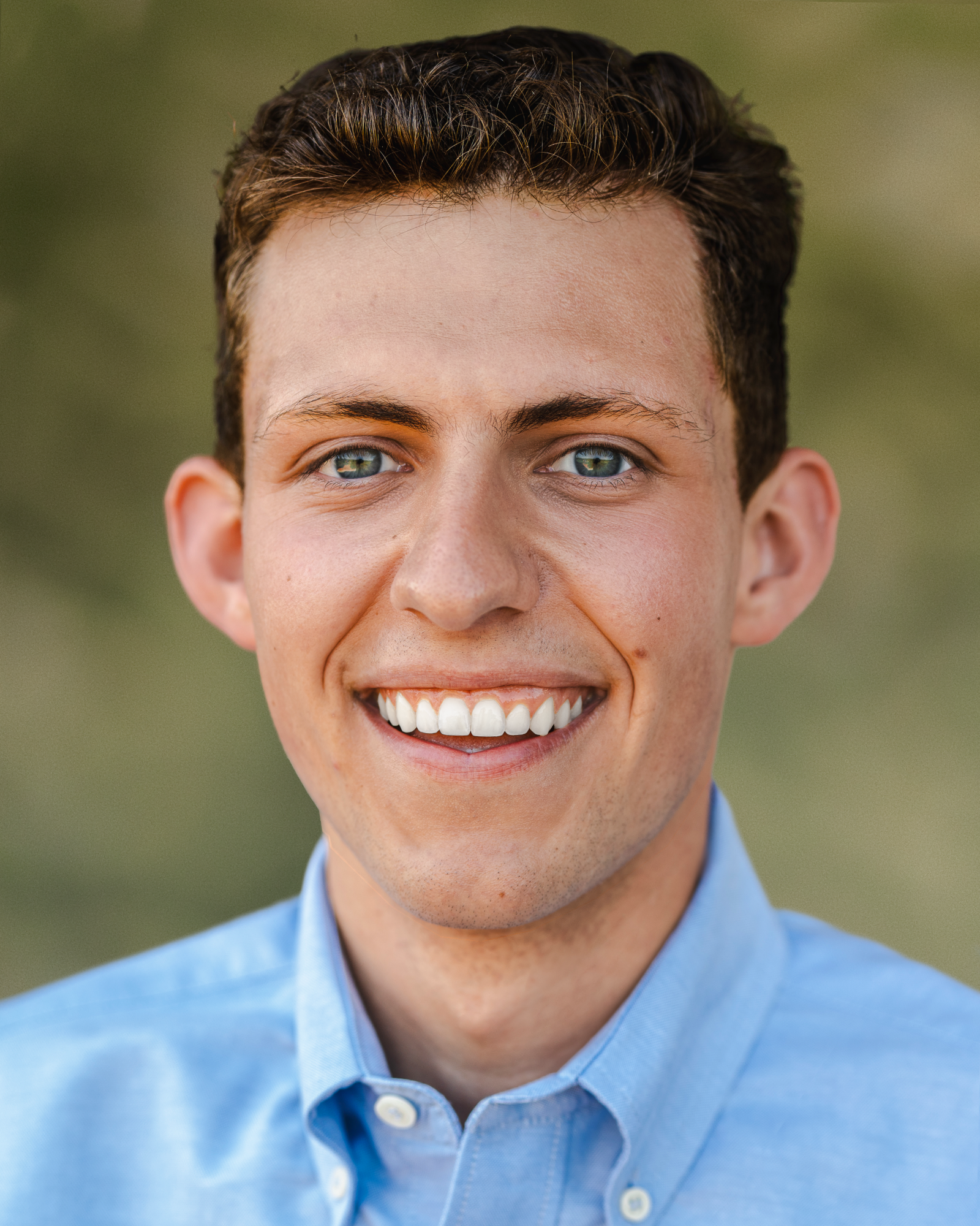 Portrait of Charlie Fahey wearing a light blue button-down shirt against a softly blurred green background.