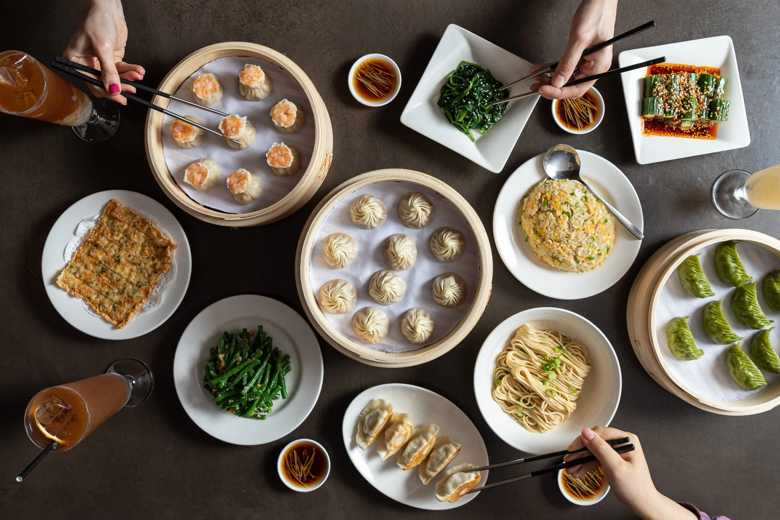 table laden with asian food from din tai fung, including xiao long bao, pancakes, greens and noodles