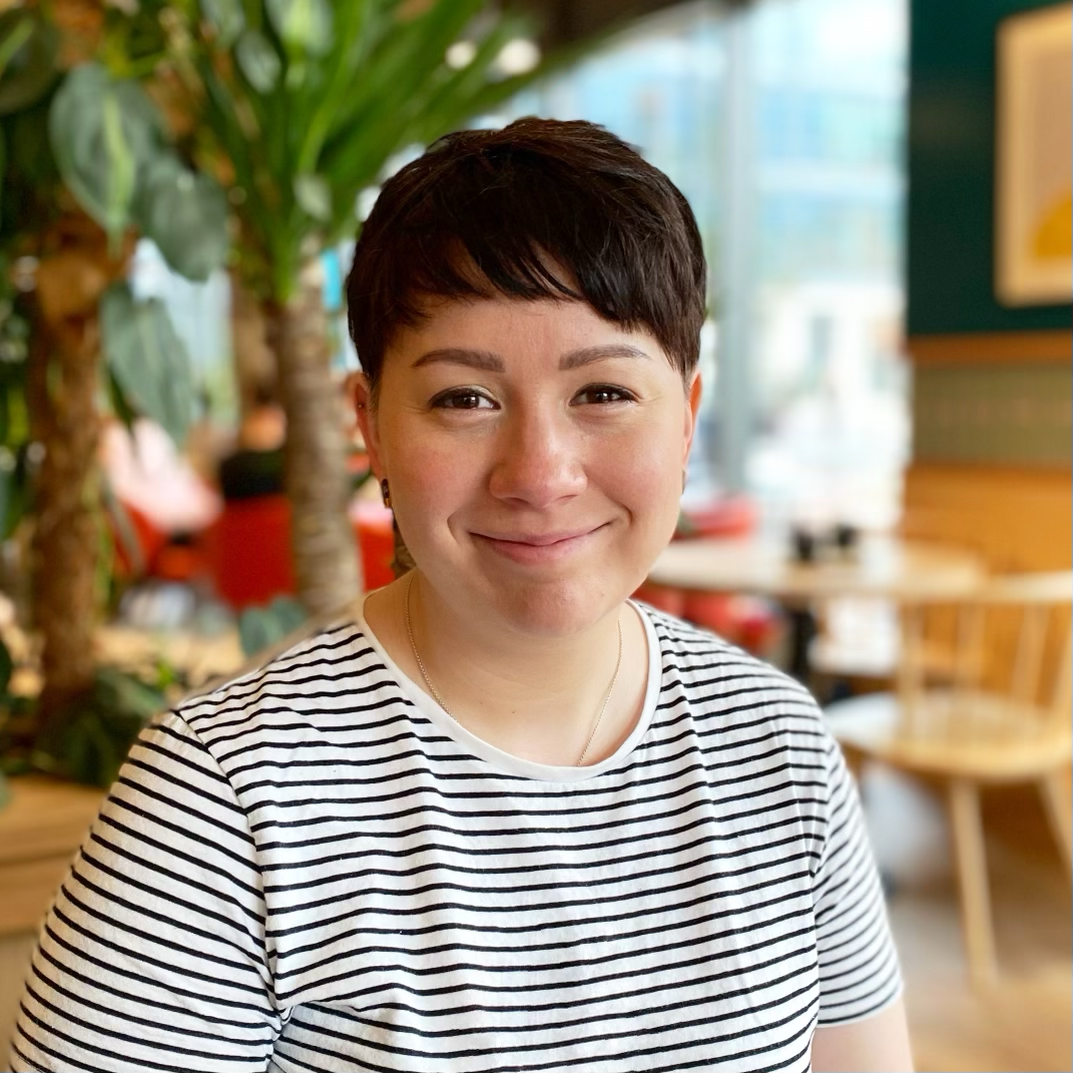 Headshot of Jess Darnes, a thirty-something white woman with short brown hair, wearing a striped t-shirt sitting in a cafe