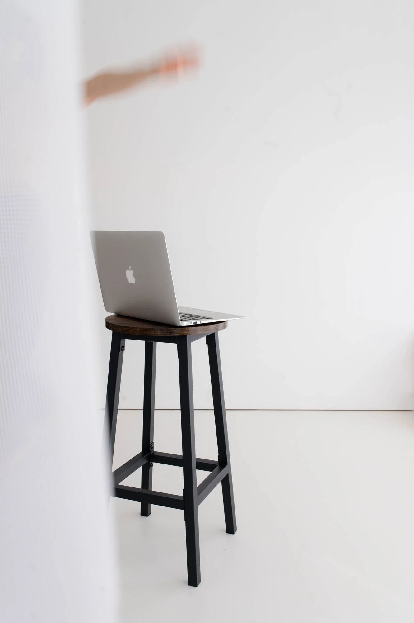 Minimalist laptop on stool with arm of Squarespace website designer coming into frame