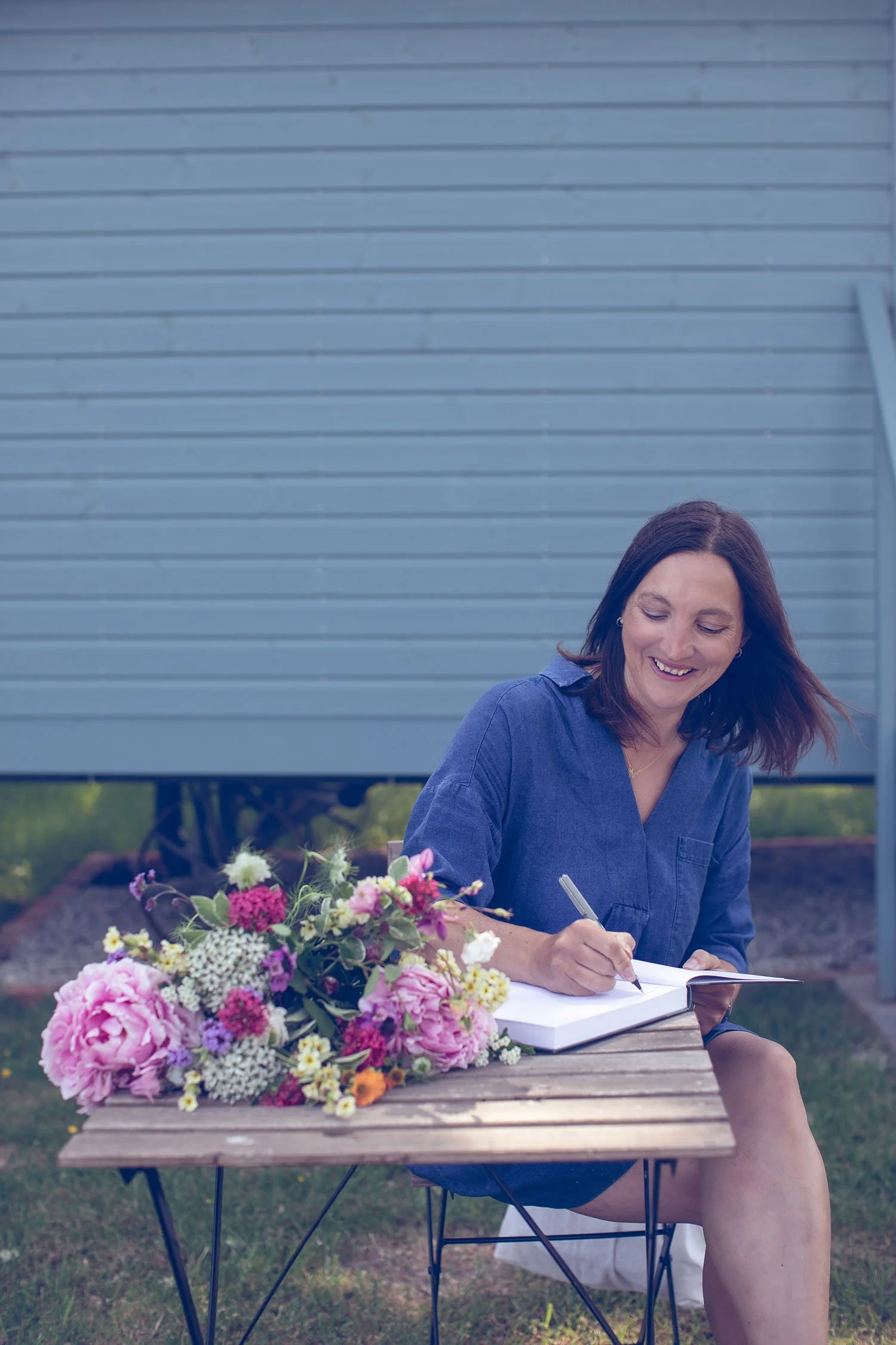 Wedding florist Jo sat at table writing in book with bouquet on table