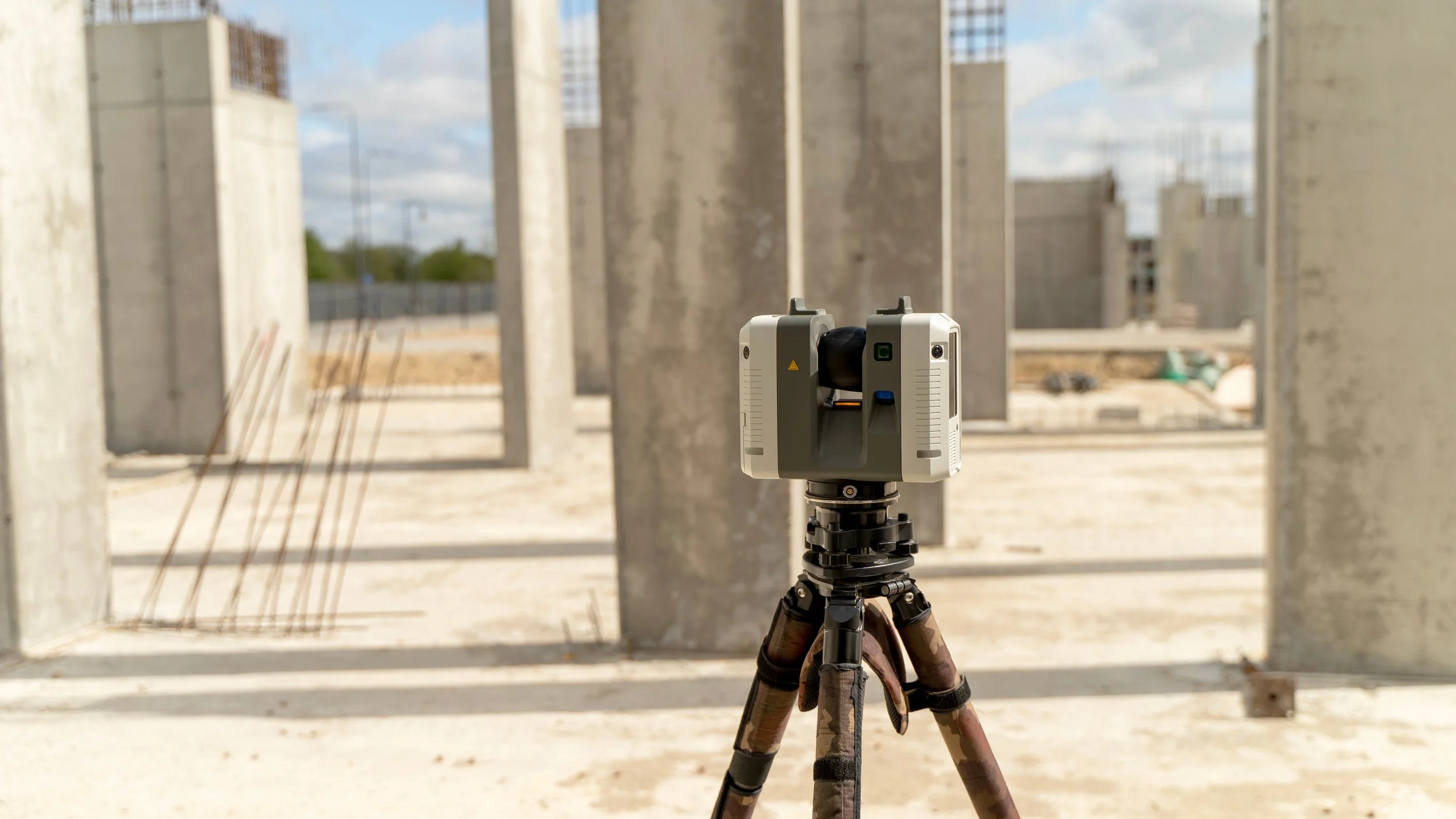 Surveying instrument on tripod at construction site with concrete columns and an open sky in the background.