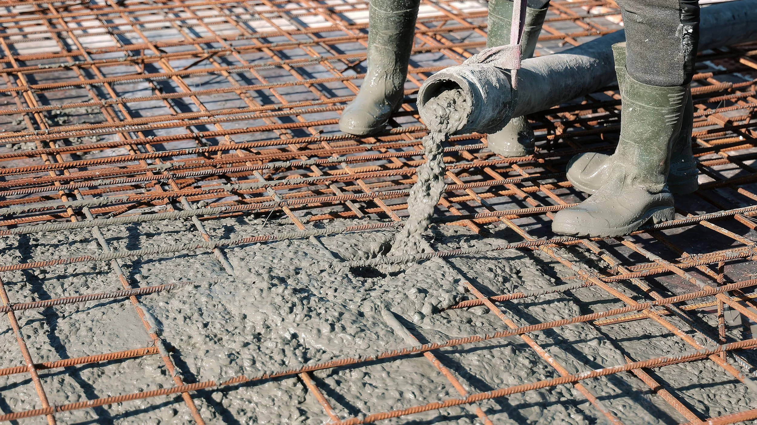 Construction worker pouring wet concrete onto a rebar grid at a construction site.