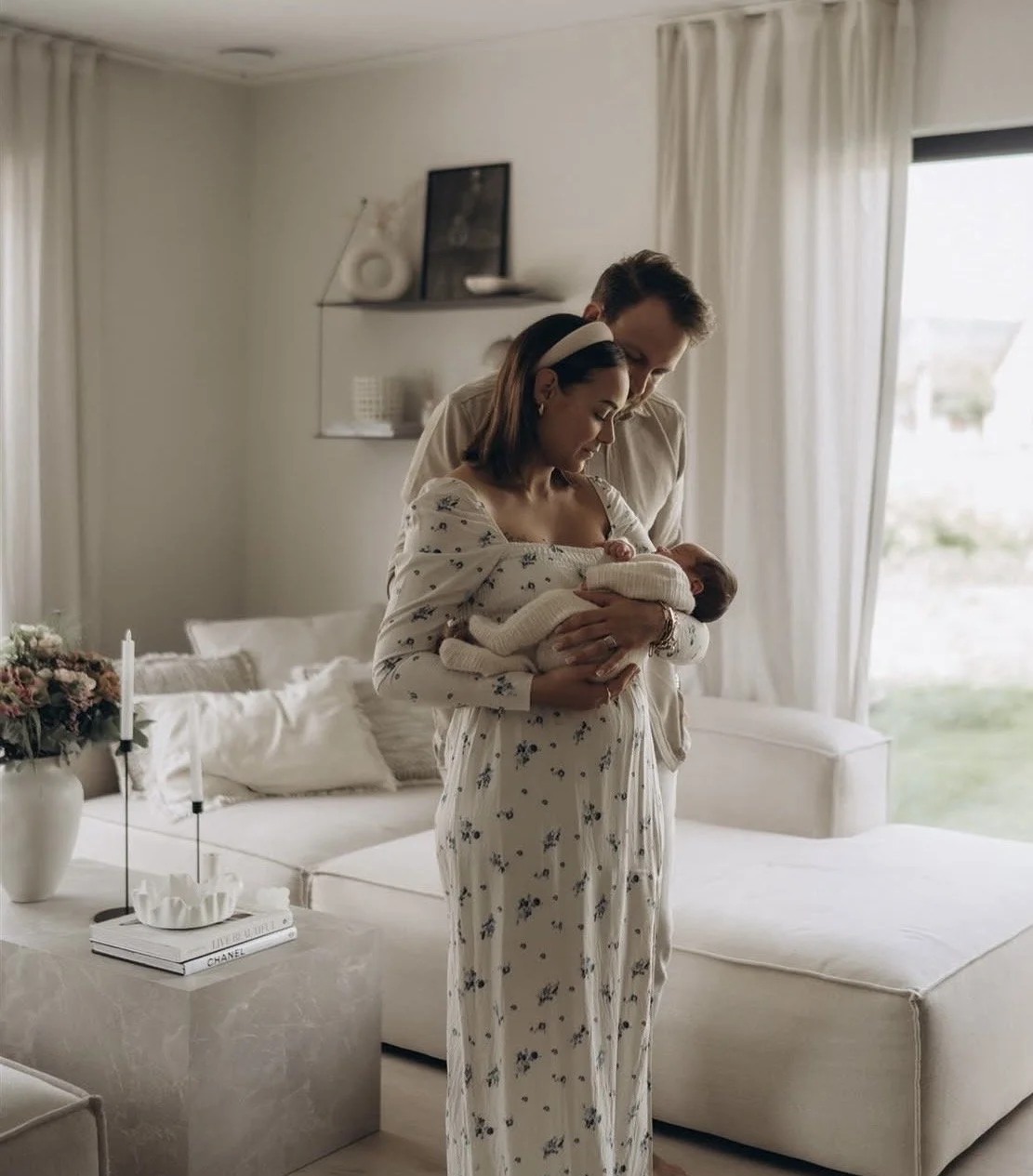 Ein Paar hält ein Baby in einem hellen, modern eingerichteten Wohnzimmer.