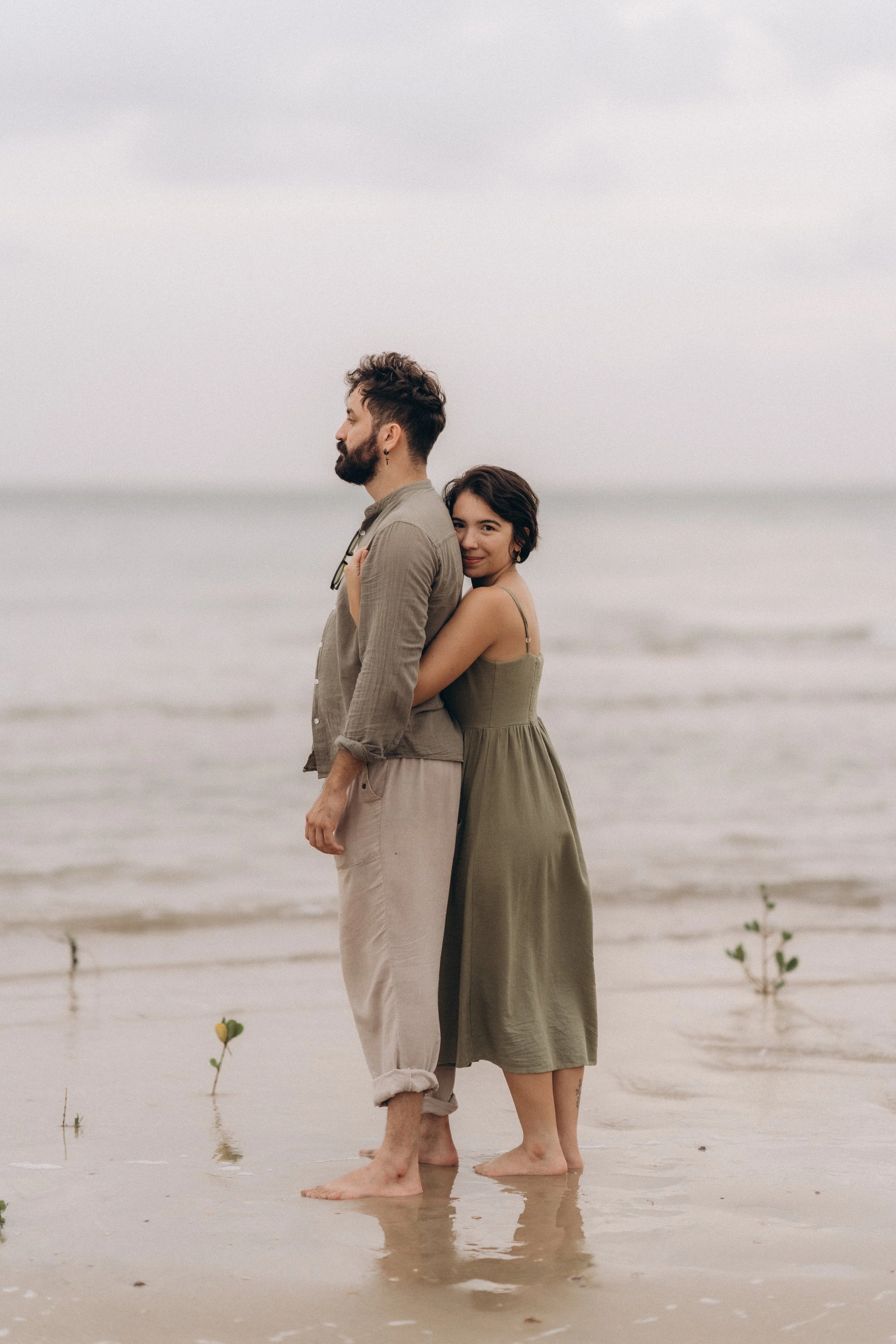 Ein Mann und eine Frau stehen im Wasser am Strand, umarmt, mit Blick nach vorne, bei bewölktem Himmel.