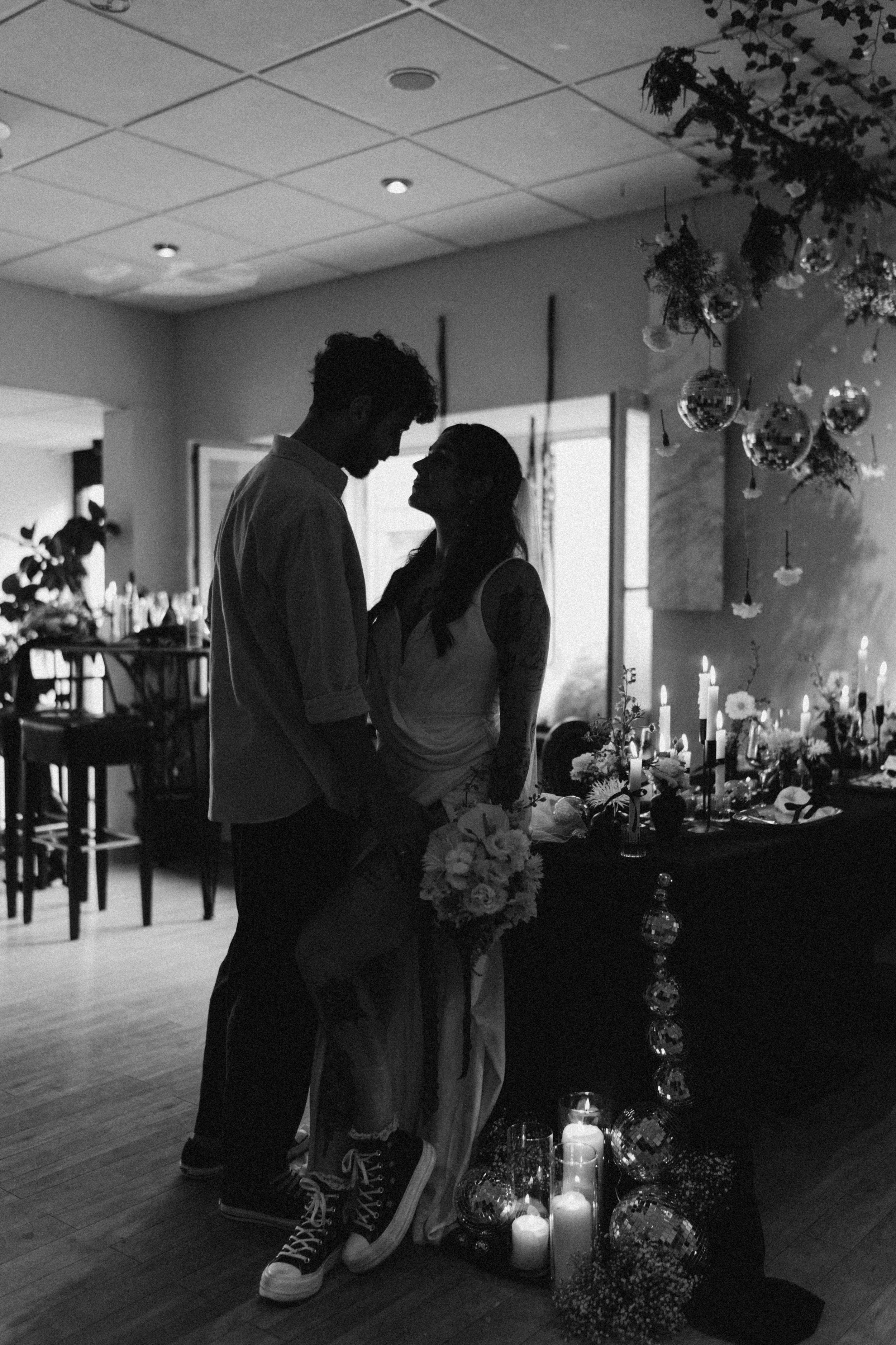 Silhouette eines Paares, das sich bei einer Hochzeit in einem festlich dekorierten Raum nahekommt, mit Kerzen und Blumen auf dem Tisch.