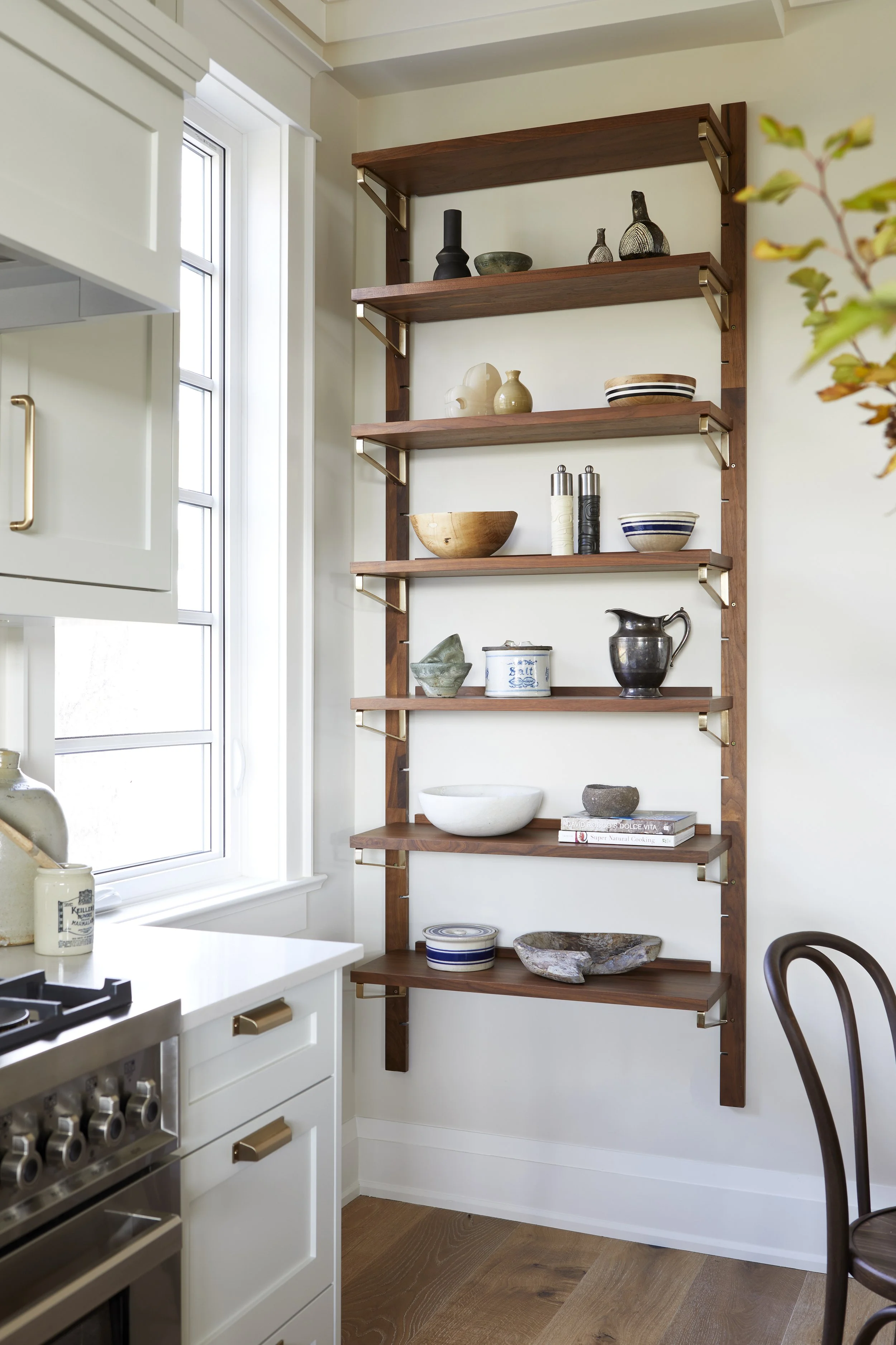 Wooden wall shelf with decorative dishes and vases in a kitchen next to a window.