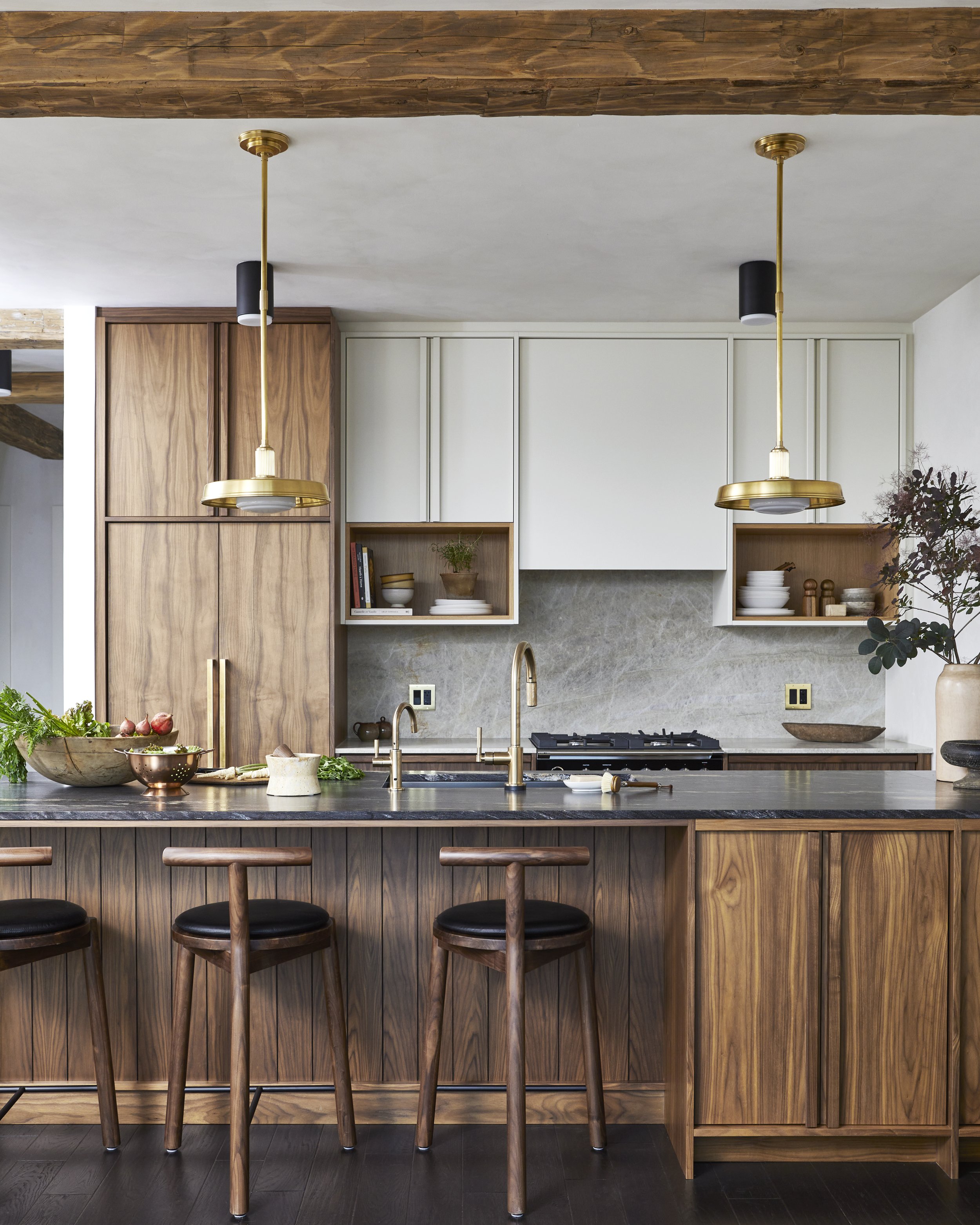 Modern kitchen with wooden cabinetry, black marble counter, gold pendant lights, and three wooden bar stools with black cushions.
