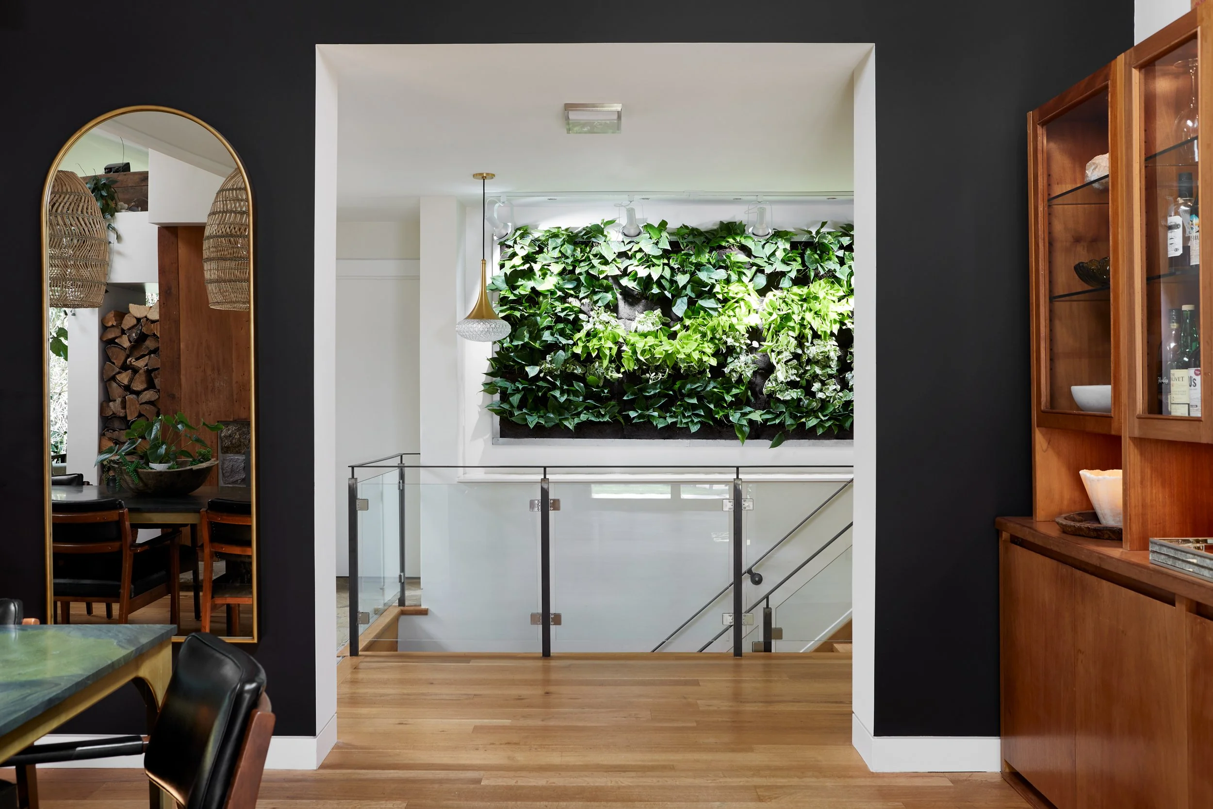 Interior view of a modern home with a green wall, wooden floors, a black wall, a glass railing, and wood cabinetry.