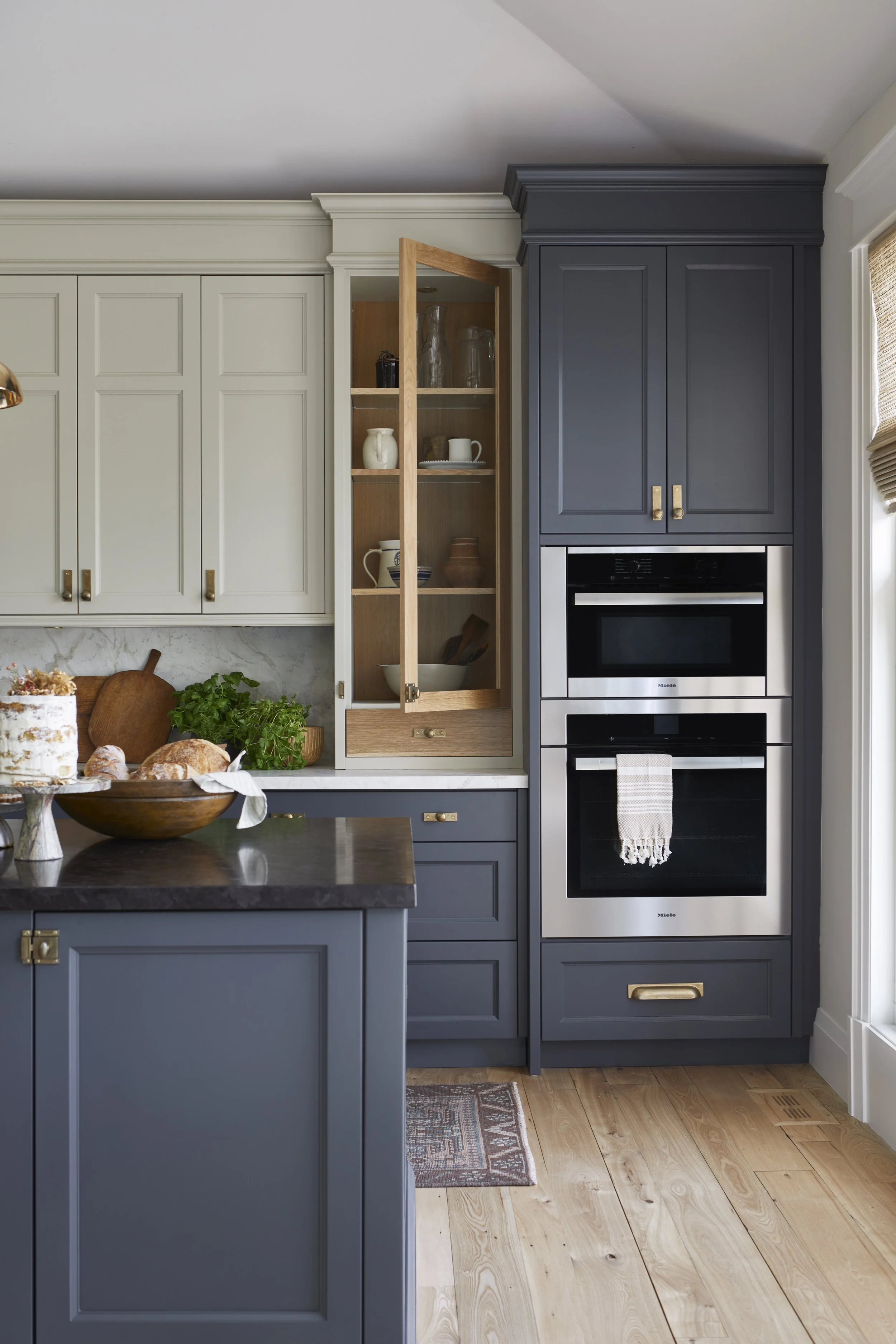 Kitchen with blue and white cabinets, open wooden shelf with dishes, double oven, and wooden floor.