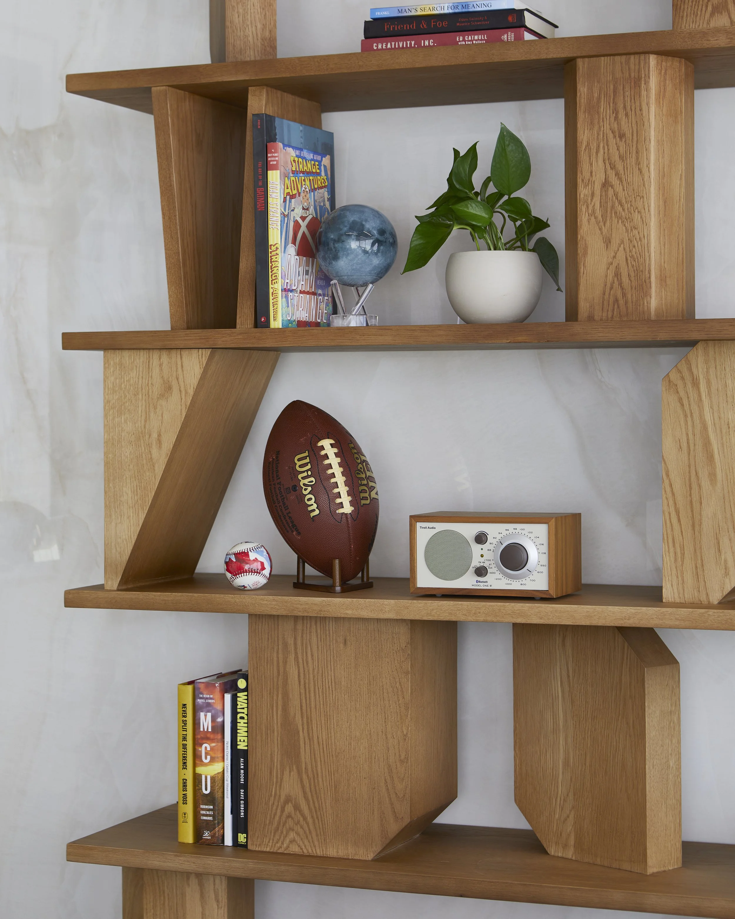 Wooden bookshelf with books, a potted plant, a decorative globe, a football, a baseball, and a vintage radio.