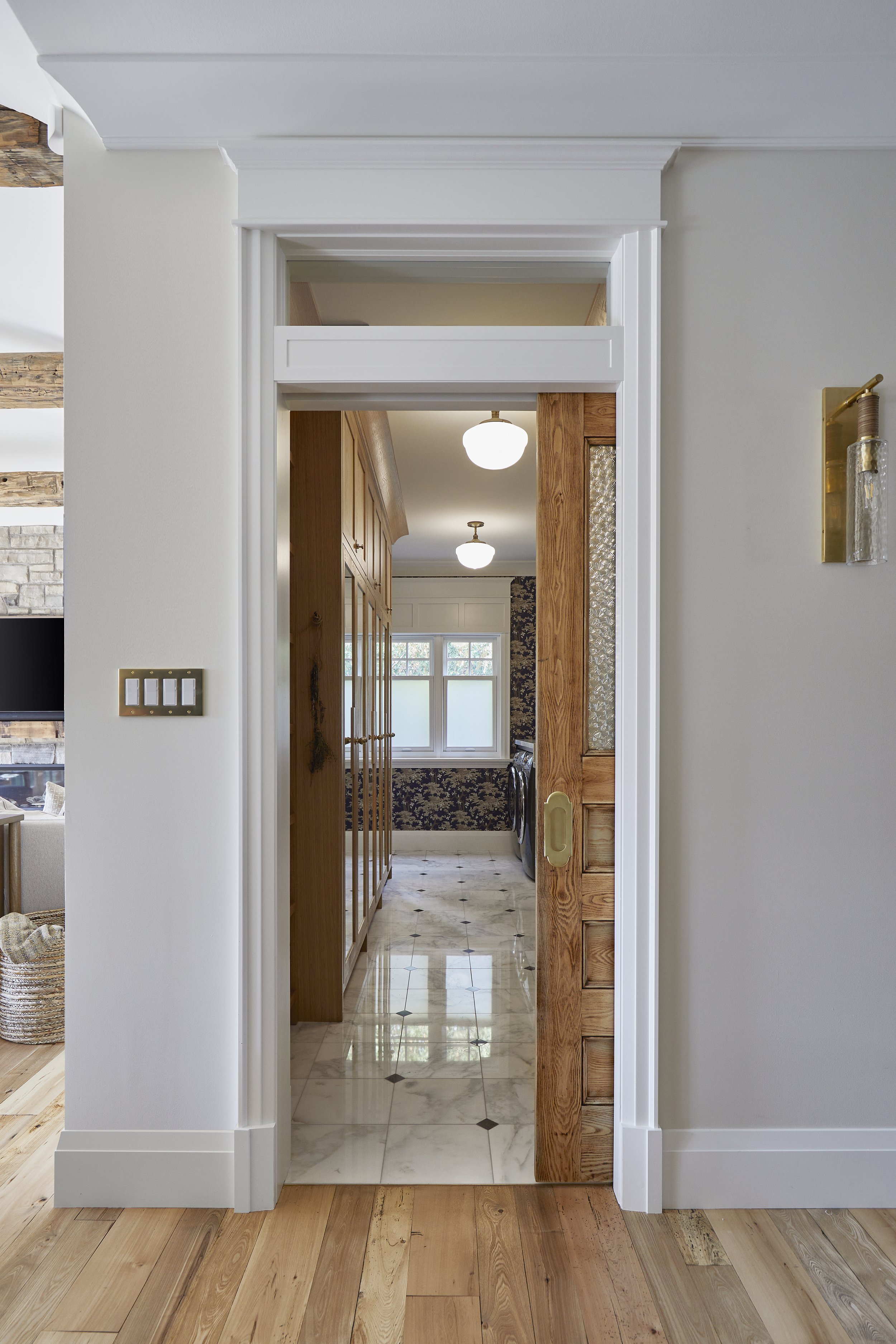 View through a door frame into a laundry room with wooden cabinets, a window, and stone tile flooring.