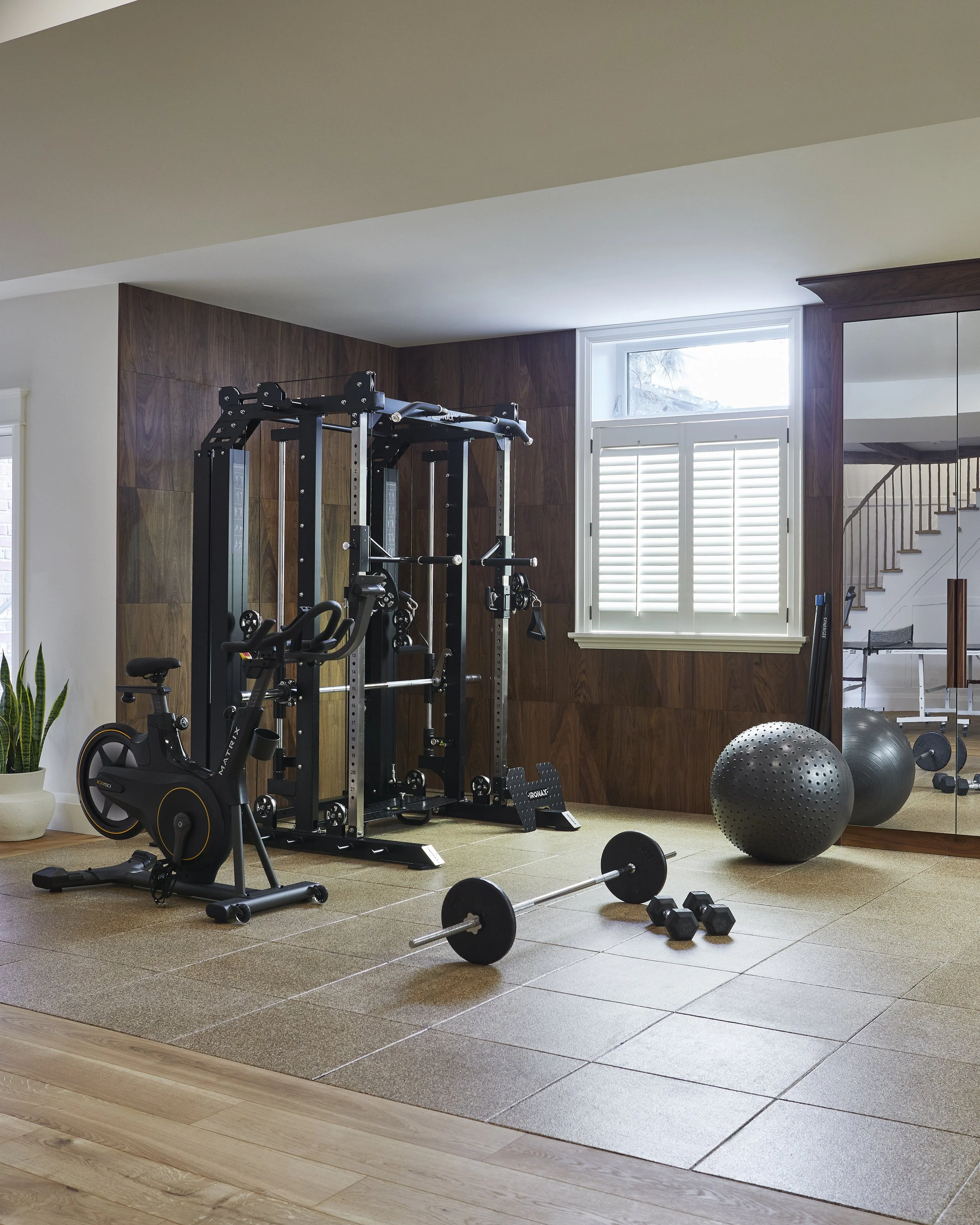 Home gym with weight machine, exercise bike, dumbbells, barbell, stability ball, and mirror.