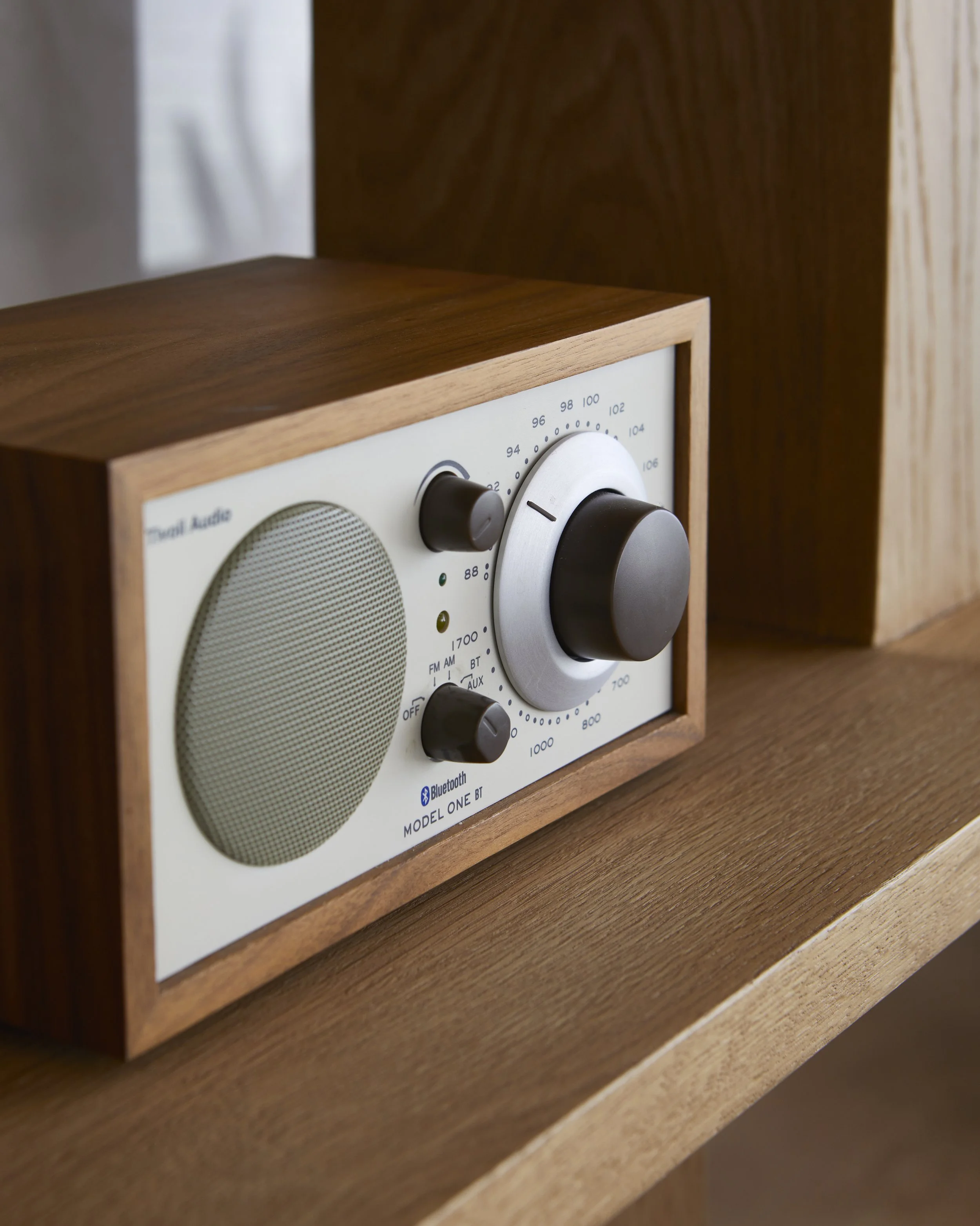 A vintage-style audio speaker with wooden casing, knobs, and tuning dial, placed on a wooden surface.