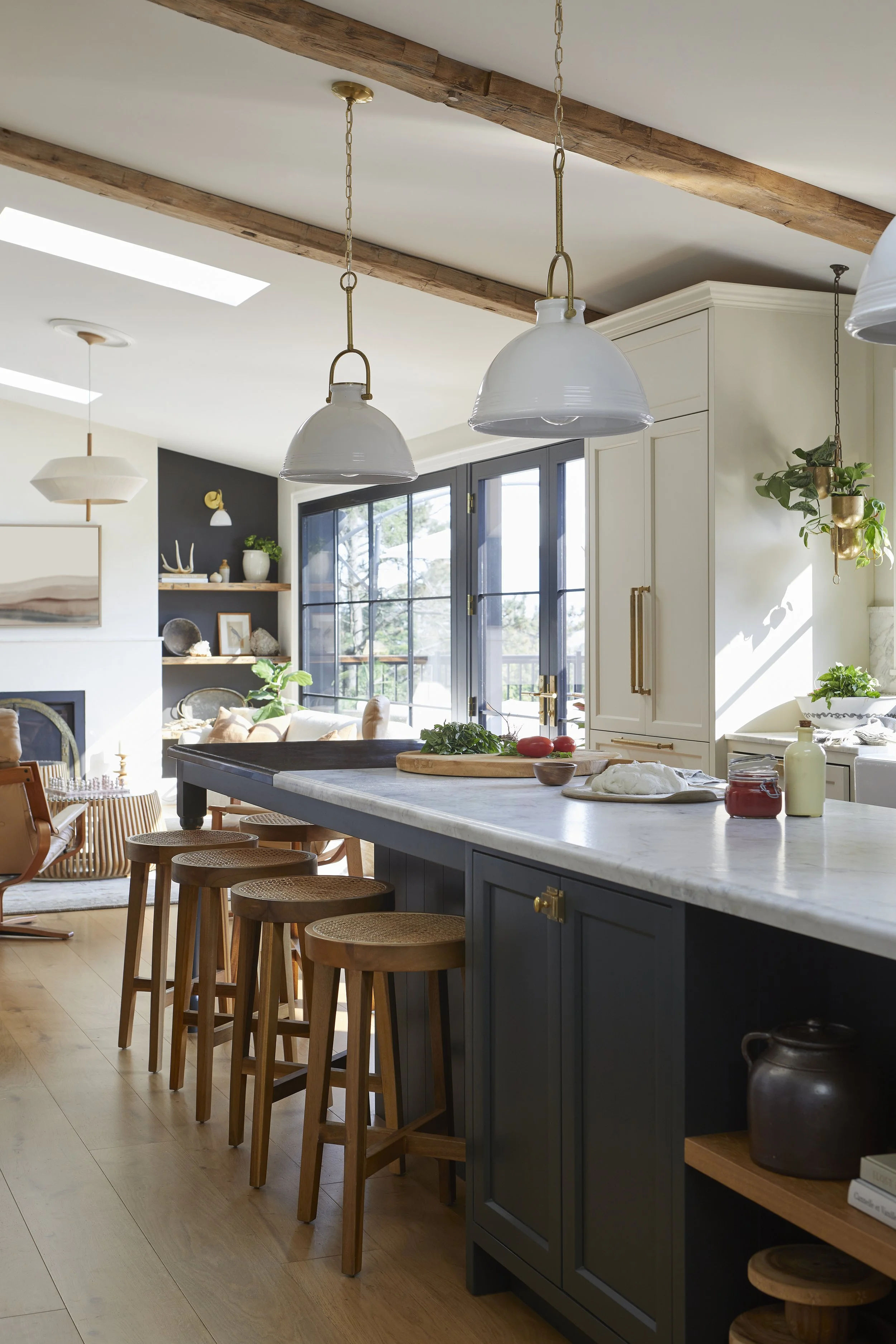 A modern kitchen with a white marble countertop, dark blue cabinets, hanging white pendant lights, and wooden barstools.