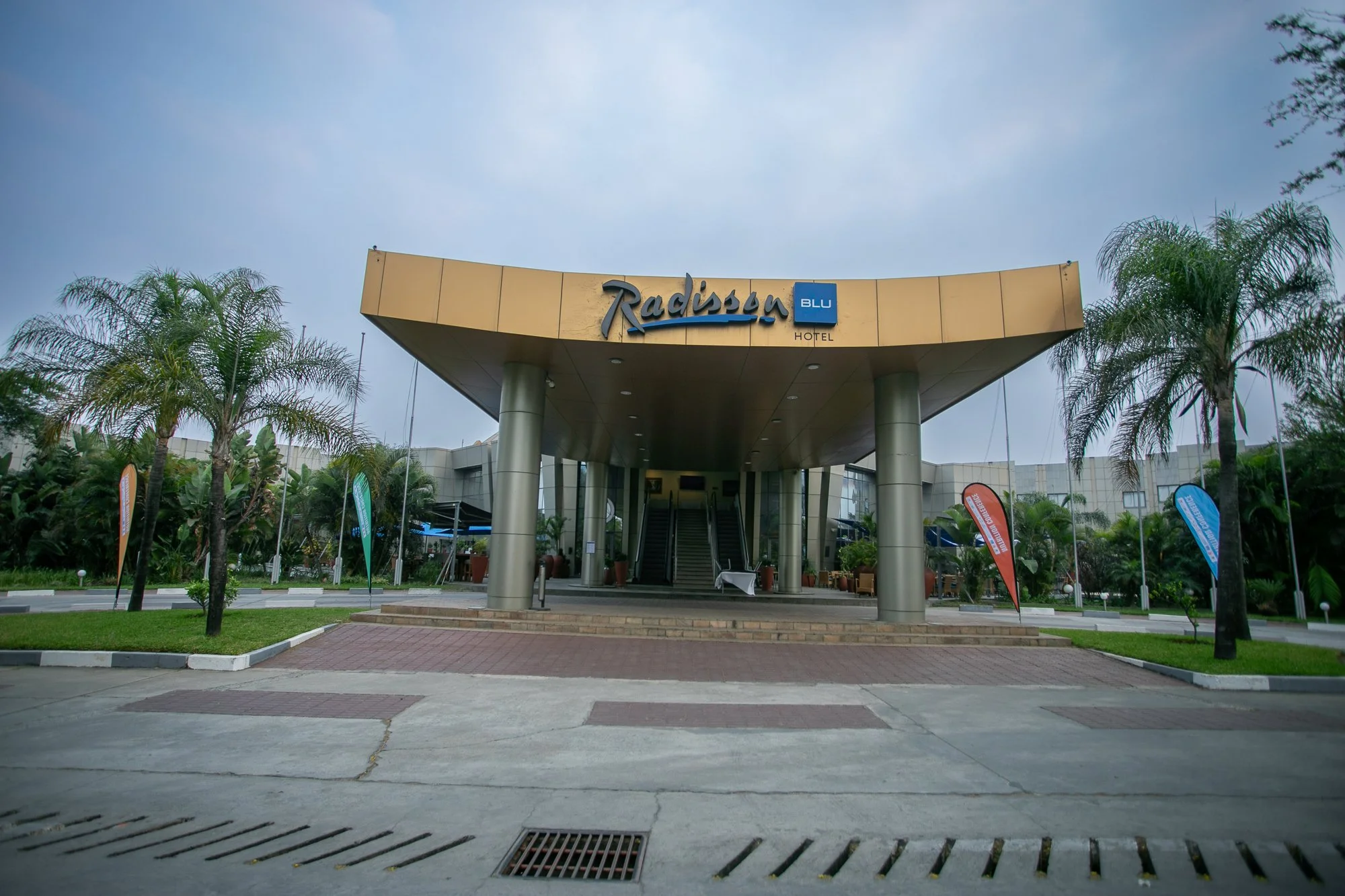 Entrance of a Radisson Blu Hotel with a canopy, palm trees, and flags in front.