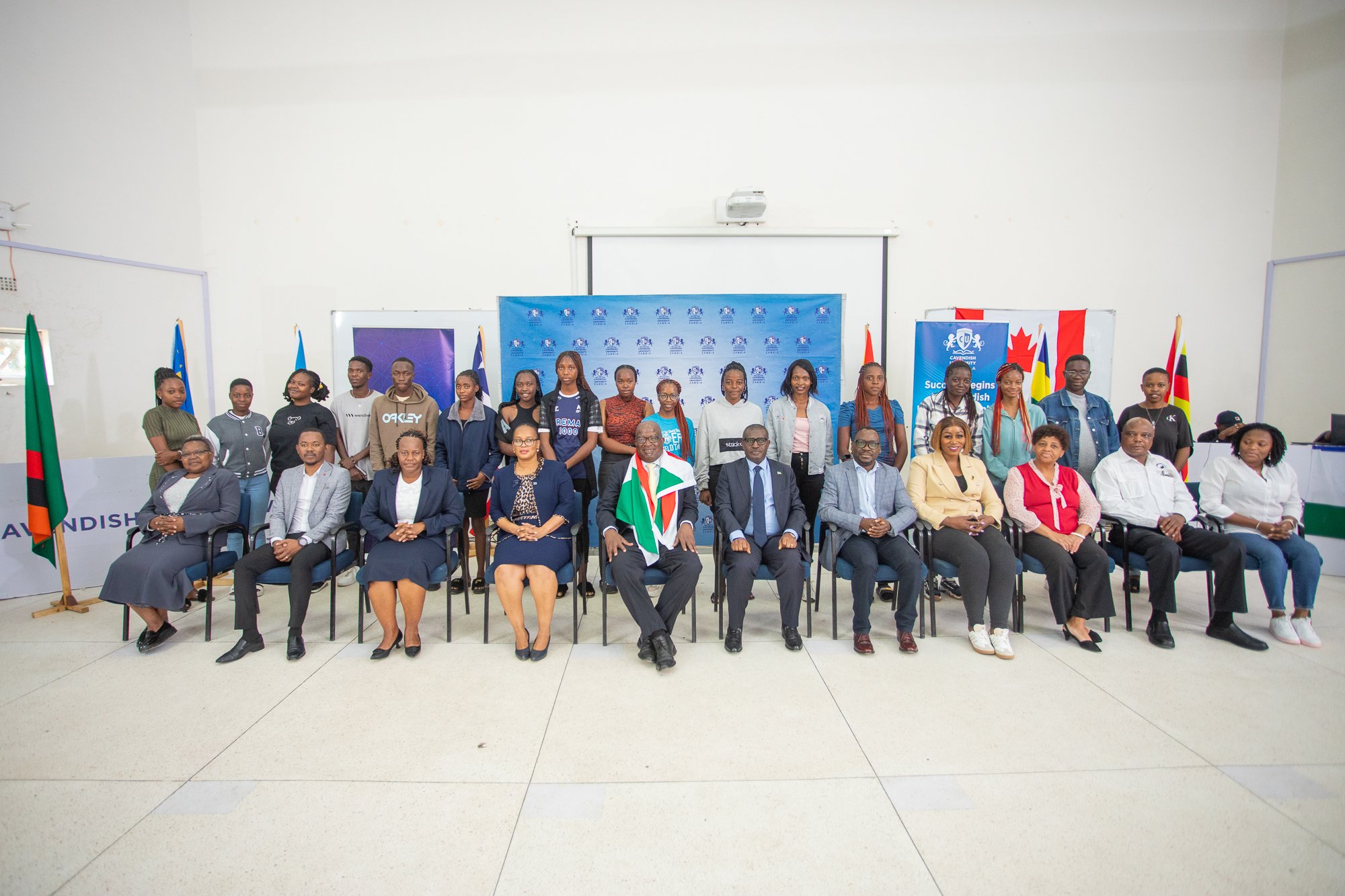 Group photo of people, including men and women, some sitting and some standing, in a room with flags and banners related to South Africa and Canada, at a formal or official event.