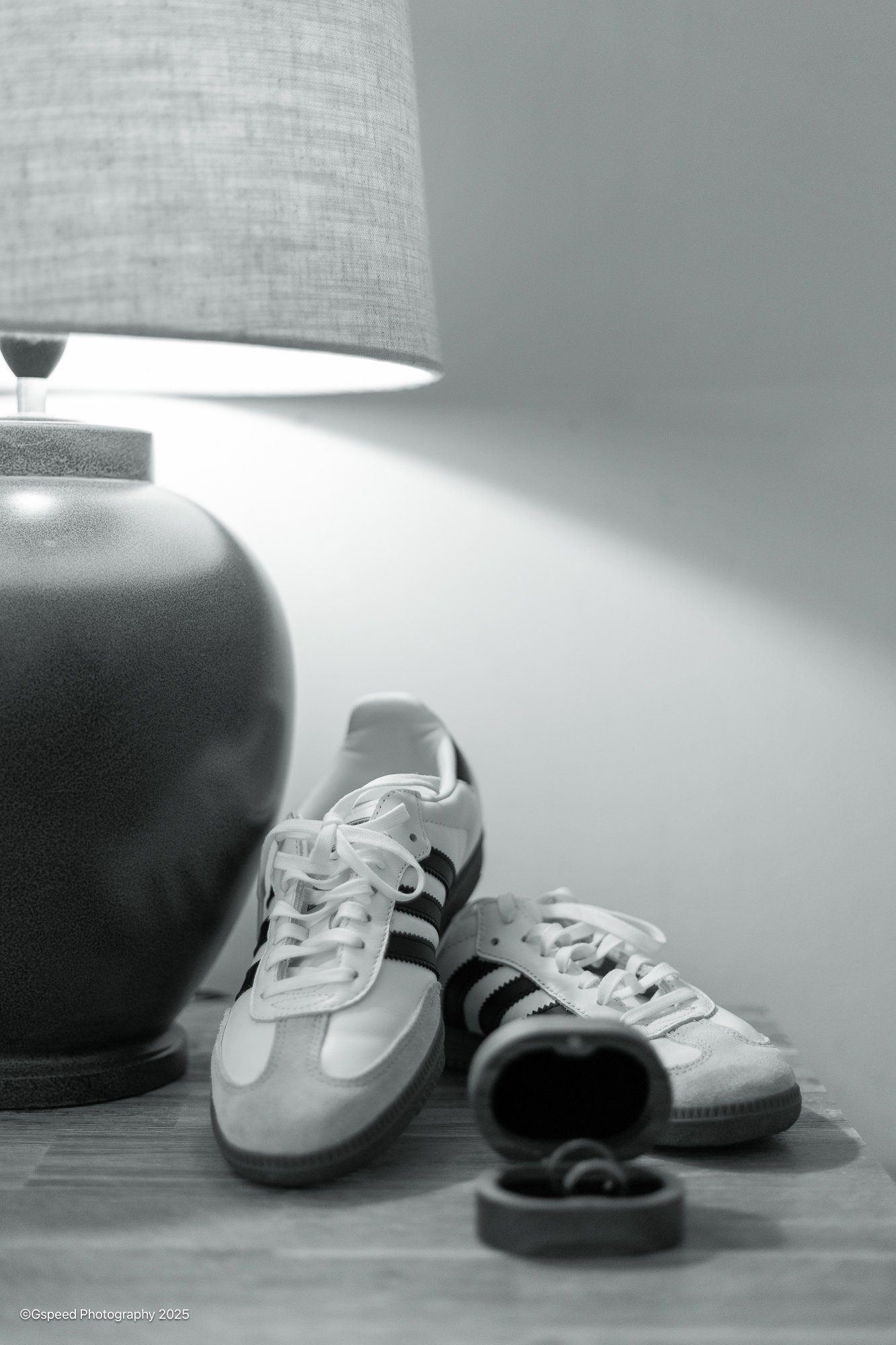 A pair of white sneakers with black stripes, a large gray exercise ball, and a pair of black dumbbells on a wooden floor near a wall, with a gray lampshade visible in the background.