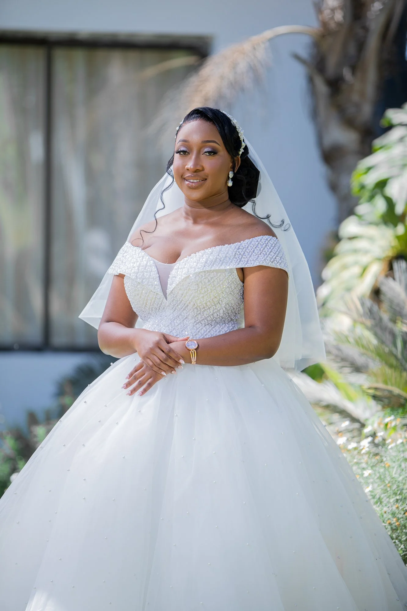 A woman in a wedding dress standing outdoors with a gentle smile.