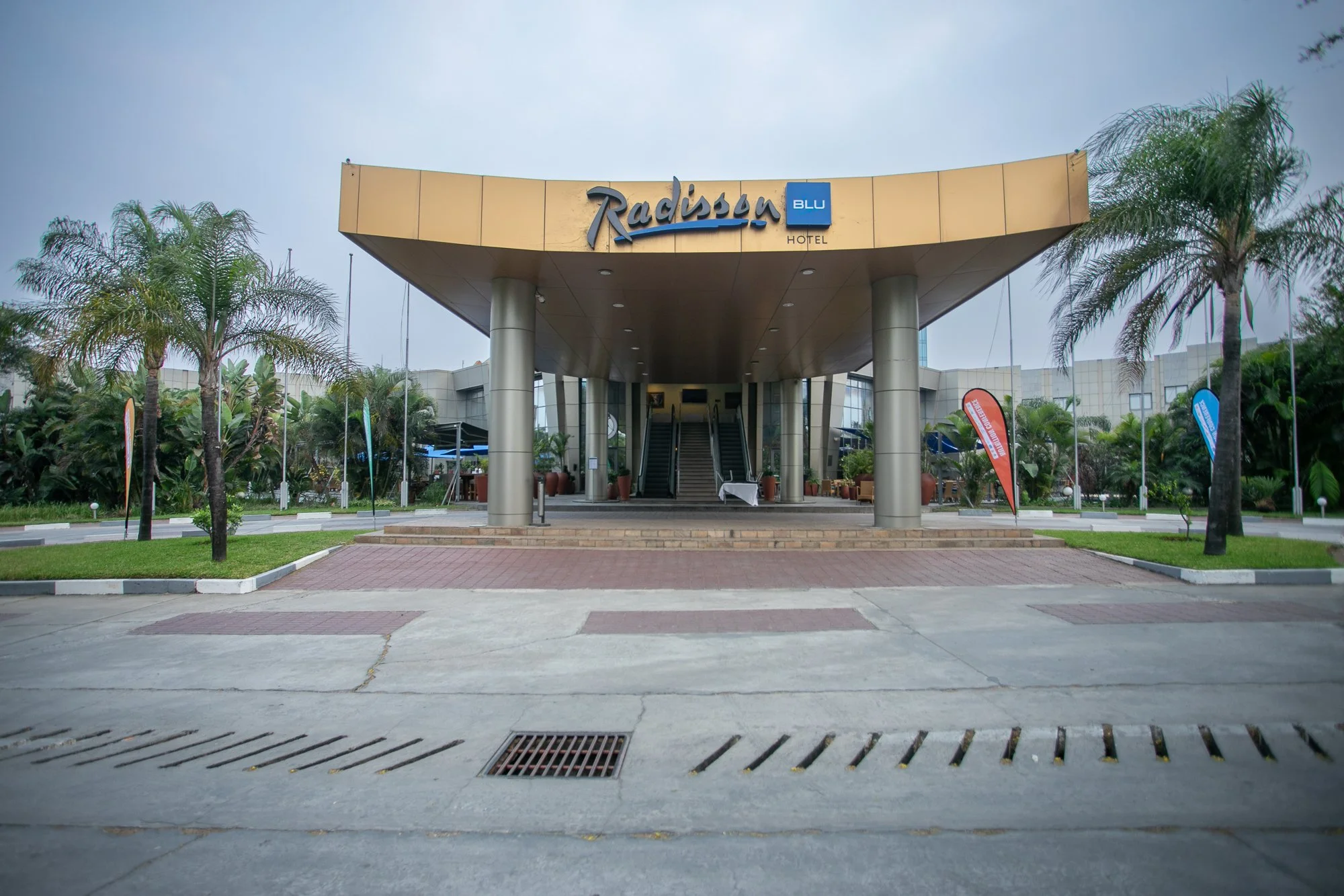 Exterior view of Radisson Blu Hotel with palm trees, a staircase, and a cloudy sky.