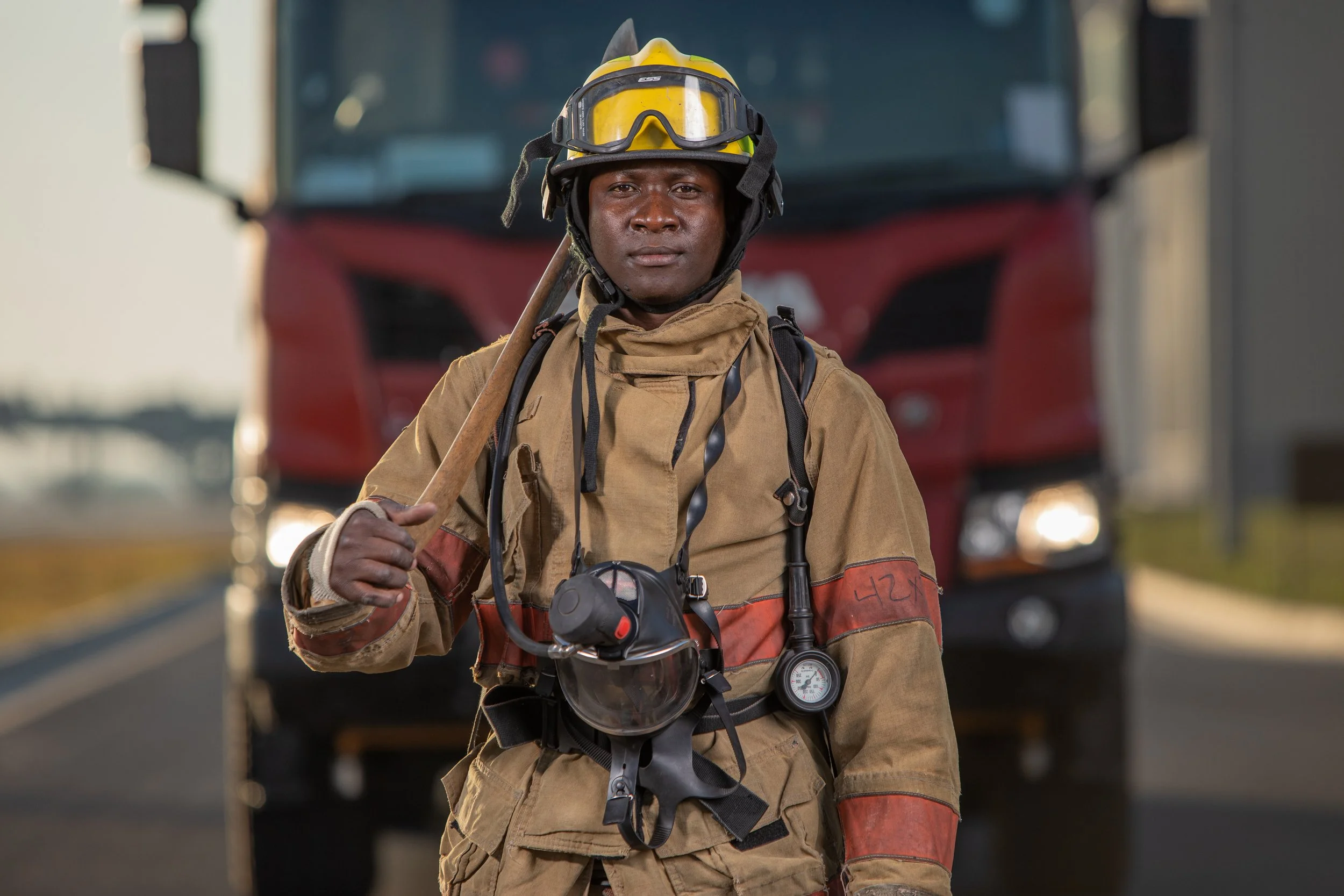 A firefighter in full gear holding an axe on a street in front of a fire truck.