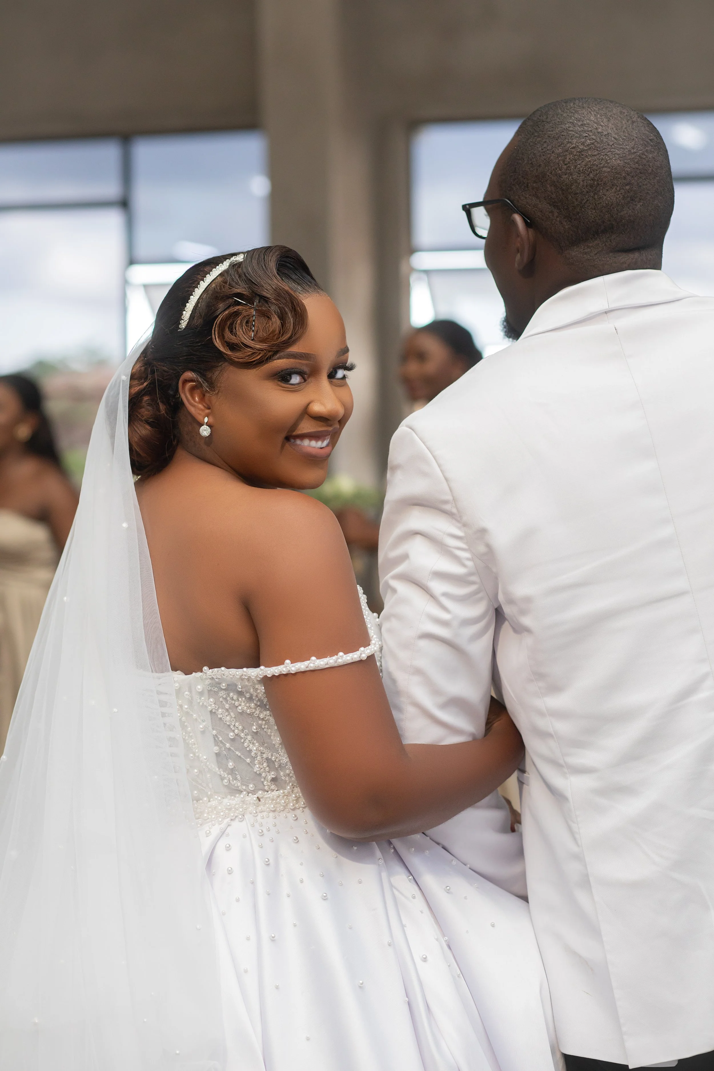 A wedding couple with the bride smiling at the camera and the groom facing away.