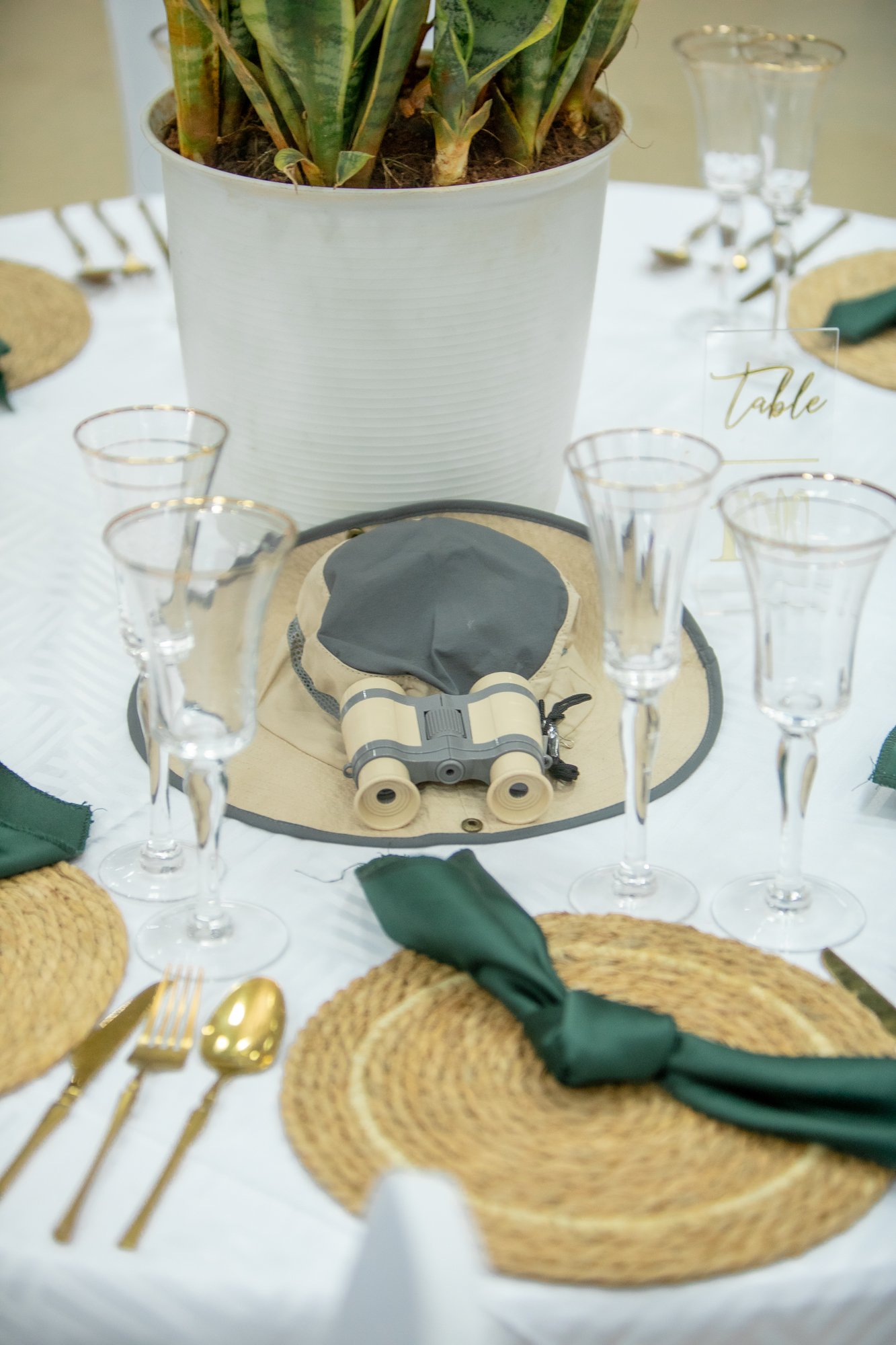 Table setting with gold utensils, green napkin, and woven placemats, decorated for an event or celebration.