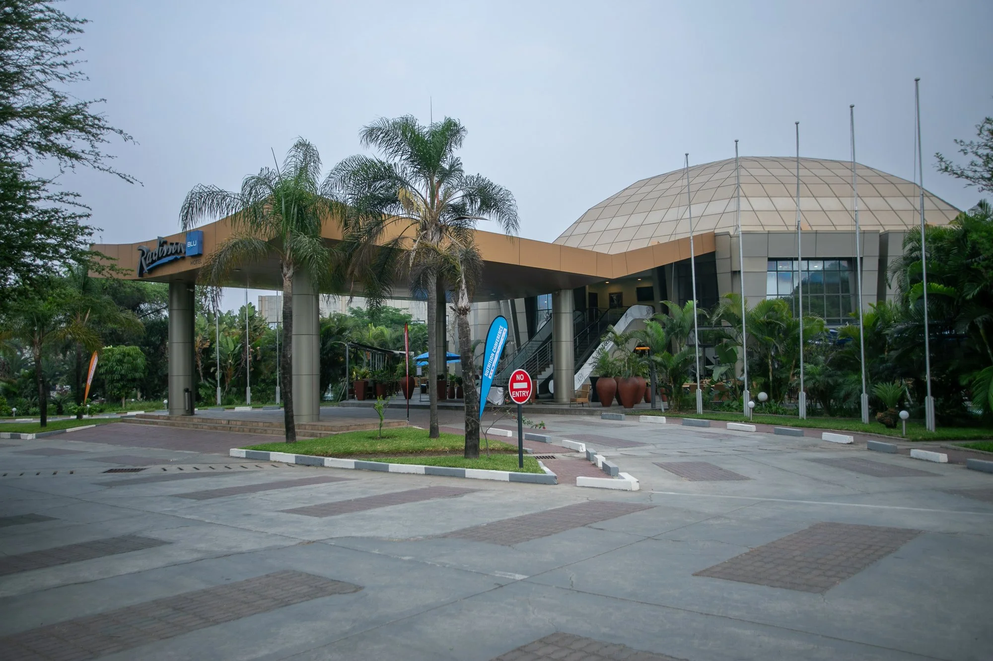 Empty parking lot with a building labeled 'Radisson Blu Hotel,' surrounded by trees and flags, under an overcast sky.