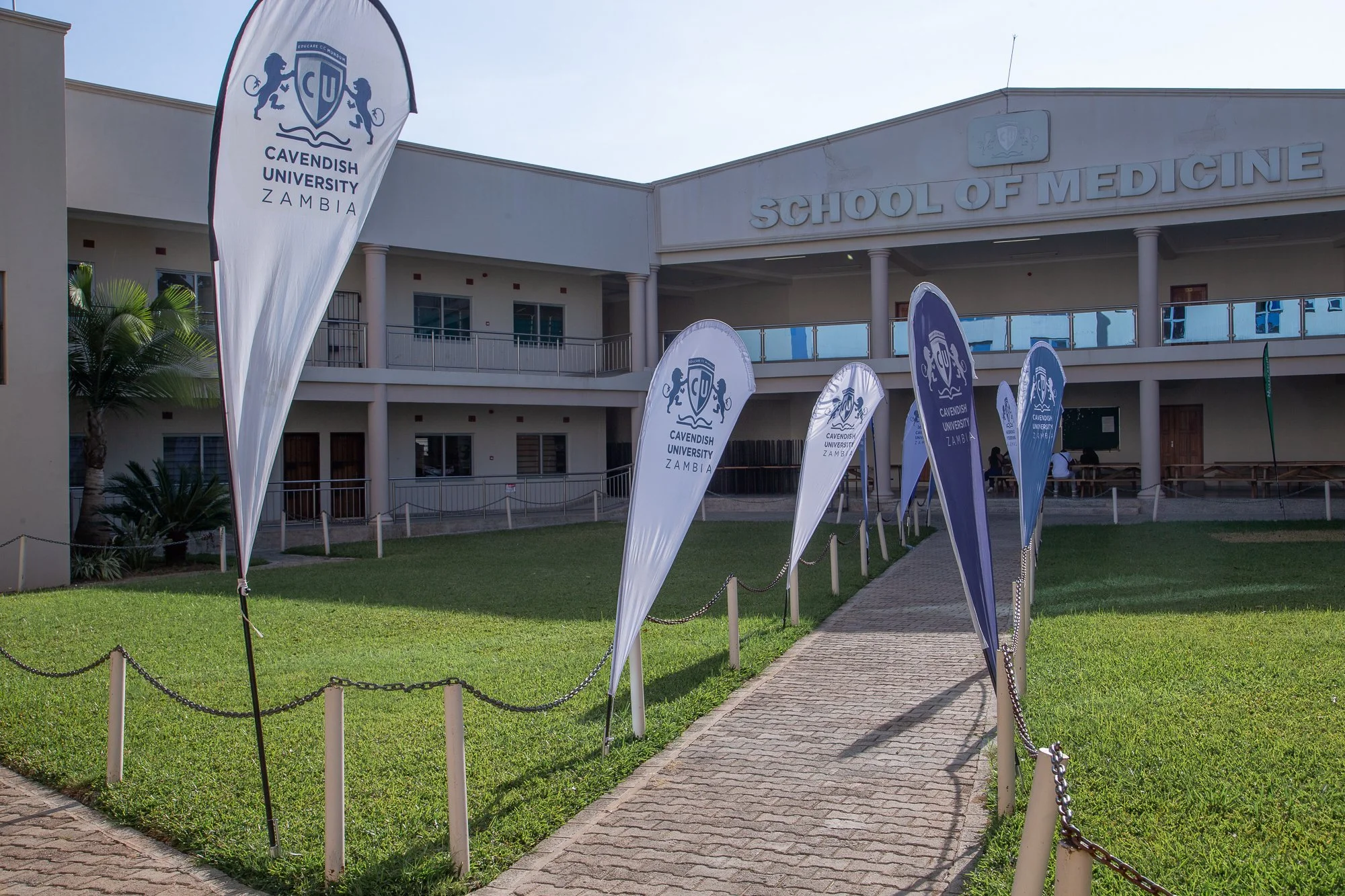A pathway leading to the Cavendish University Zambia School of Medicine building, with flags bearing the university's logo on either side.