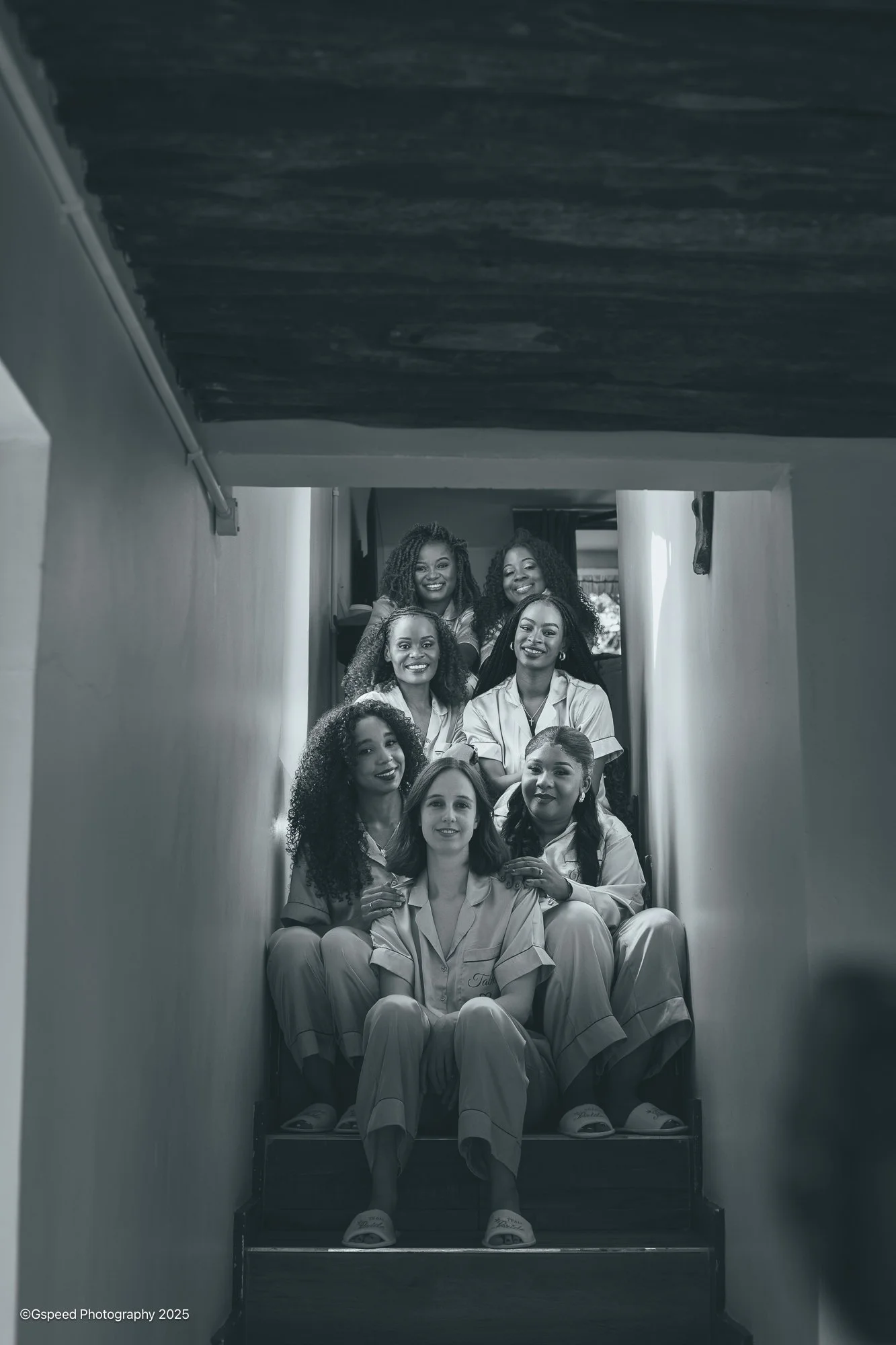 Black and white photo of eight women sitting on stairway, smiling, some with arms around each other, inside a building.
