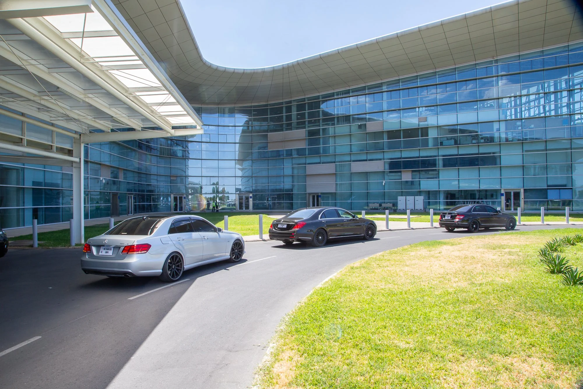Modern office building with a curved glass facade and a parking lot in front with several cars parked.