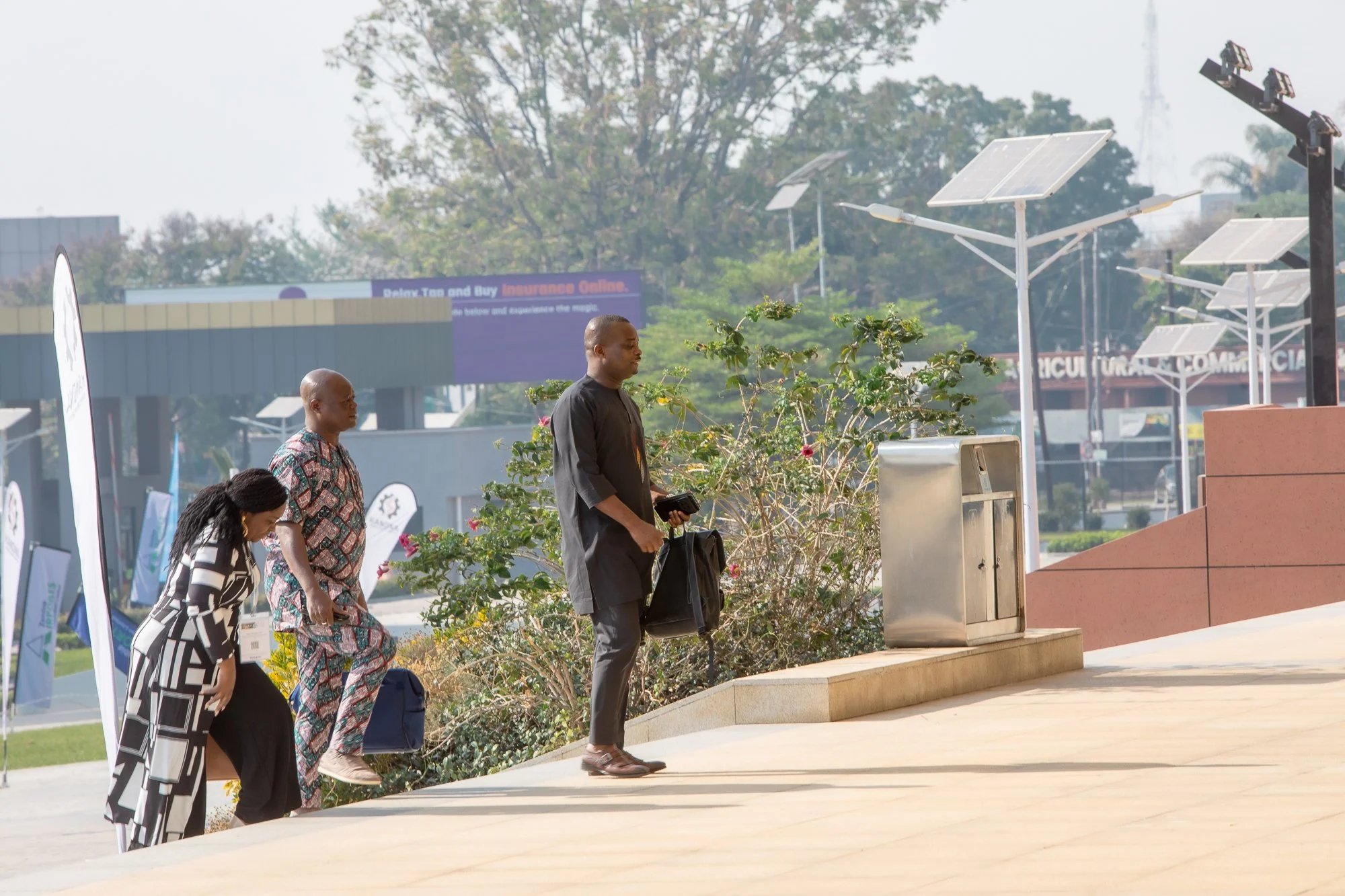 Three people walking up stairs outdoors with greenery and solar panels in the background.