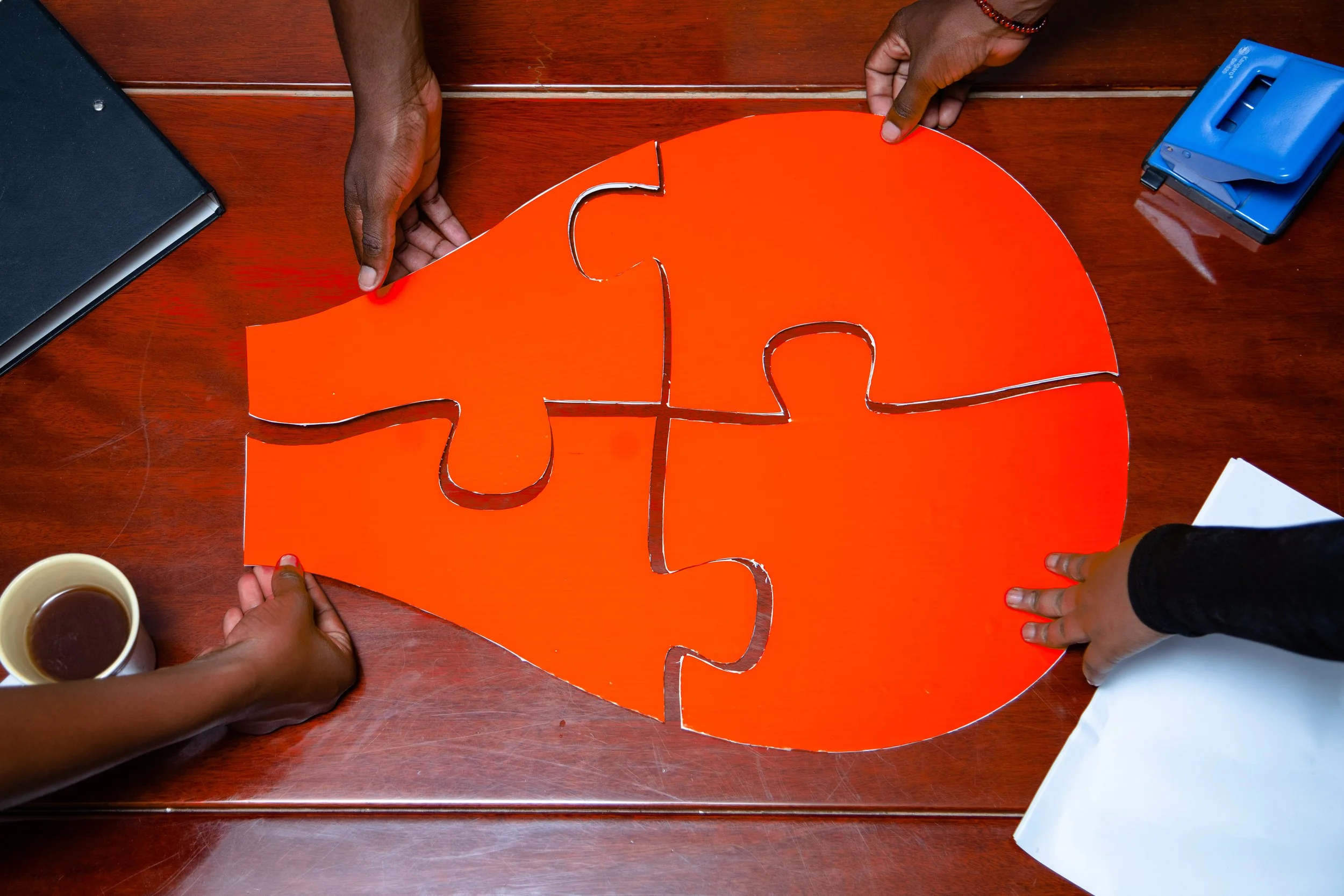 People assembling a puzzle with orange pieces on a wooden table.